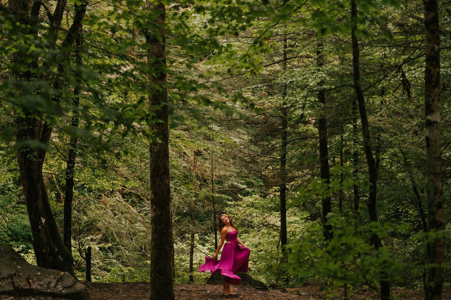 A person in a pink dress sits contemplatively on a fallen log in a lush green forest.