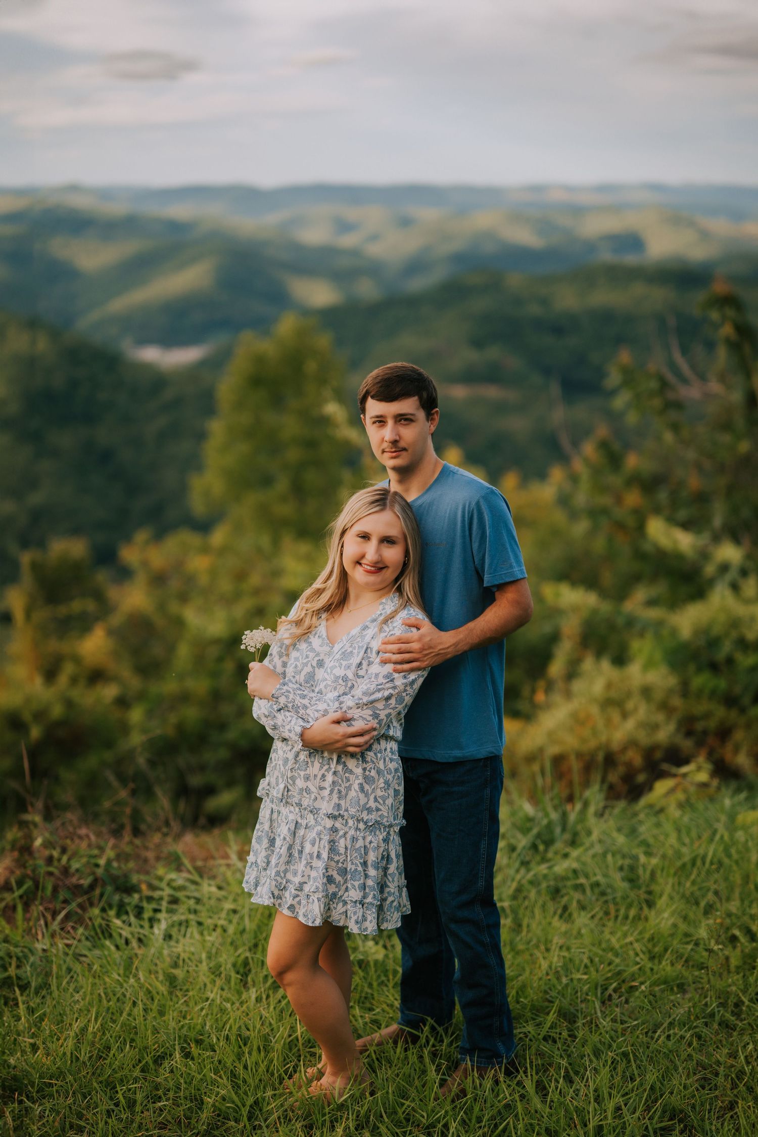 Couple posing together on a hilltop with scenic mountain views in the background.