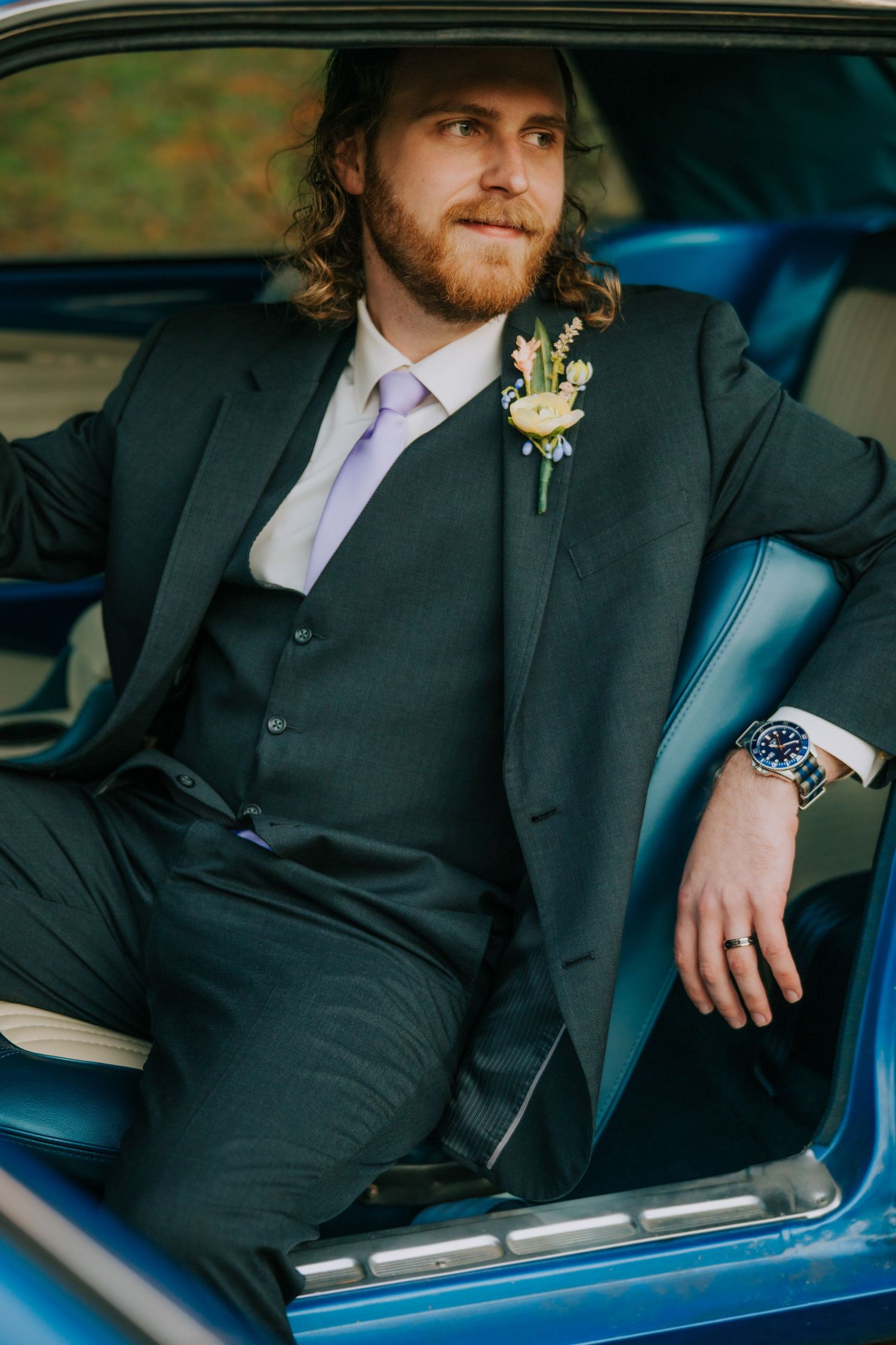 Groom in dark suit sitting in vintage blue car.