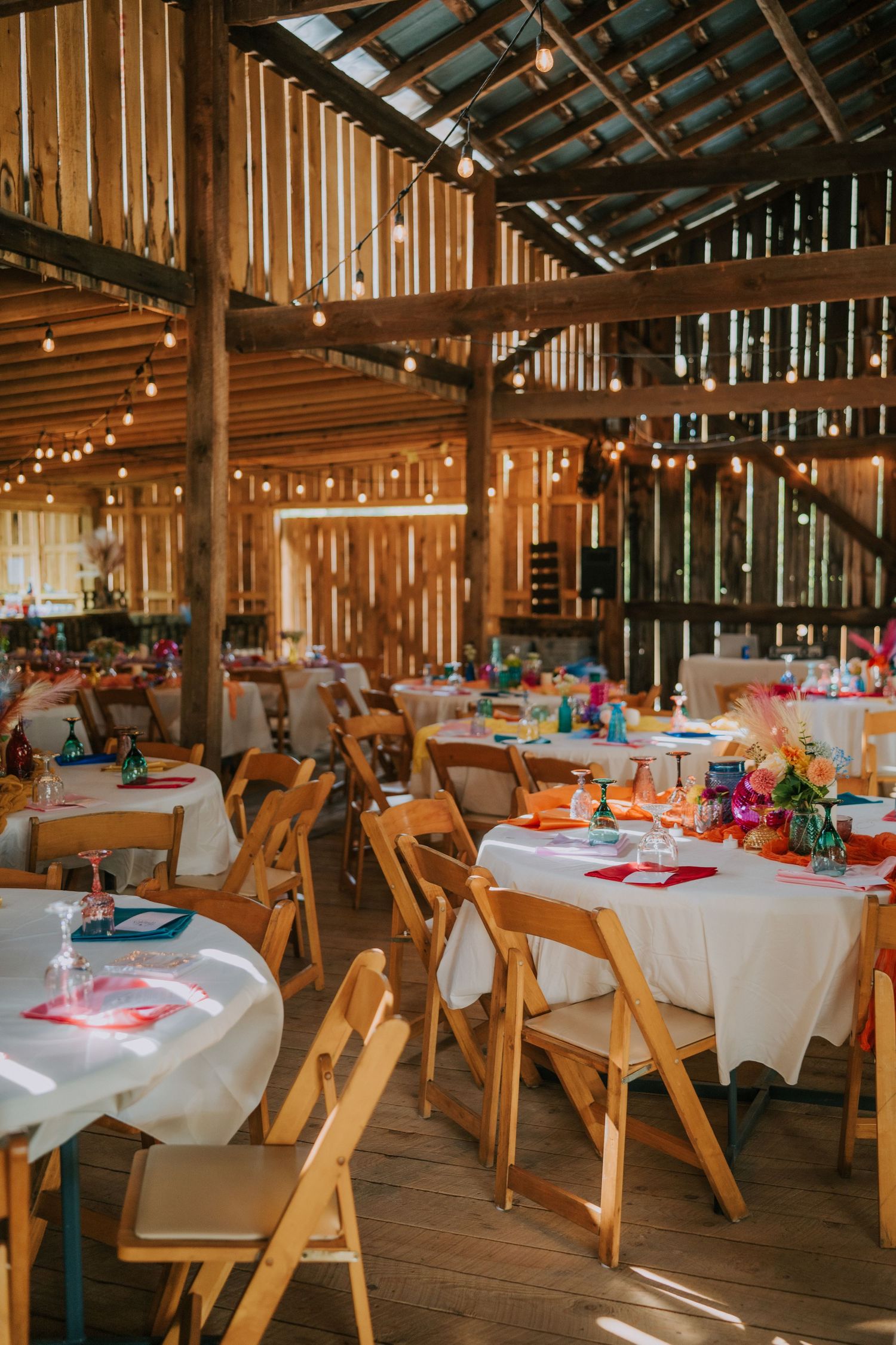 Rustic barn reception venue with wooden chairs and white tablecloths set for dinner.