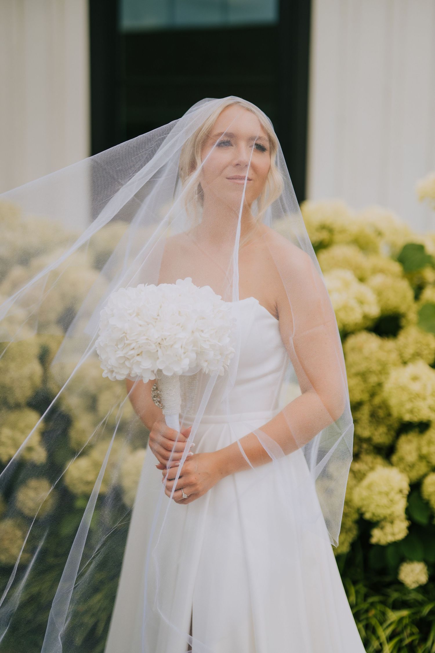 A bride in a flowing white wedding dress with a delicate lace veil against yellow flowers.