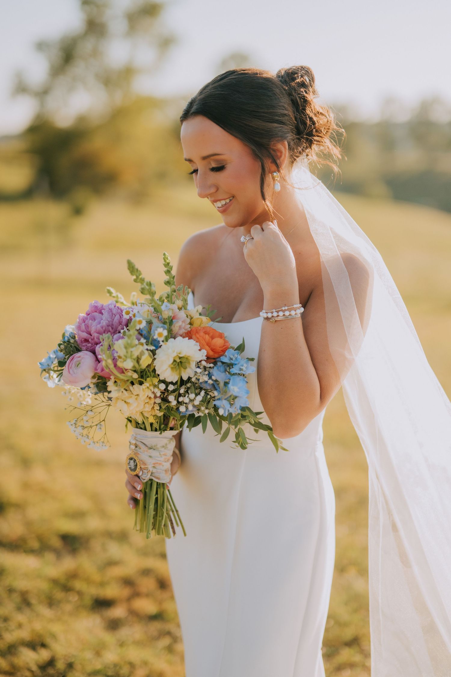 Bride holds colorful wildflower bouquet in golden sunset light during outdoor portraits.