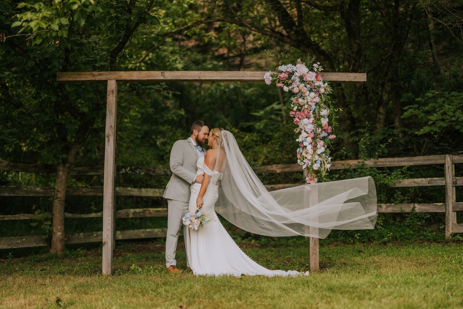 Wedding ceremony site with flowing white fabric and floral arrangements in a natural setting.