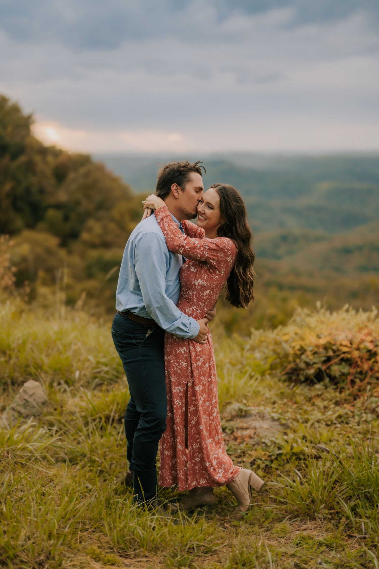 A romantic embrace on a hilltop overlooking misty mountain valleys at sunset.
