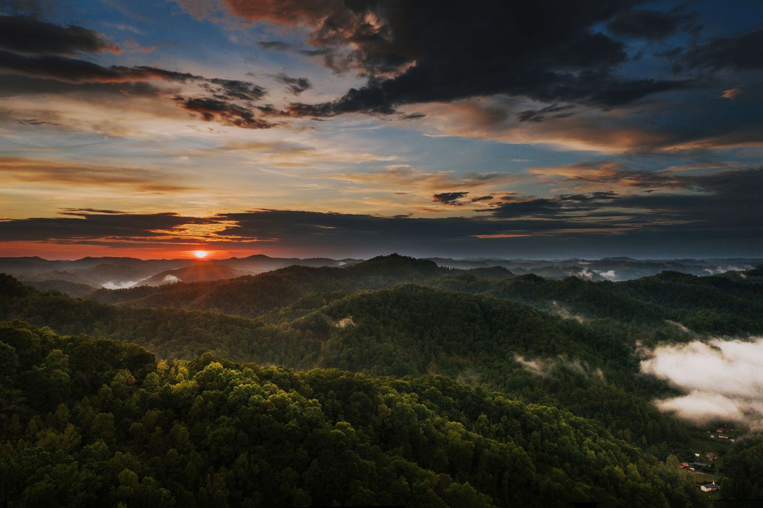Dramatic sunset over mountain ridges with colorful clouds and misty valleys.