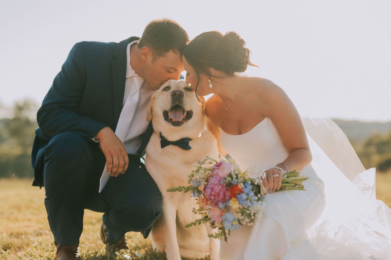 A tender wedding moment captured in warm sunlight with colorful floral bouquet details.