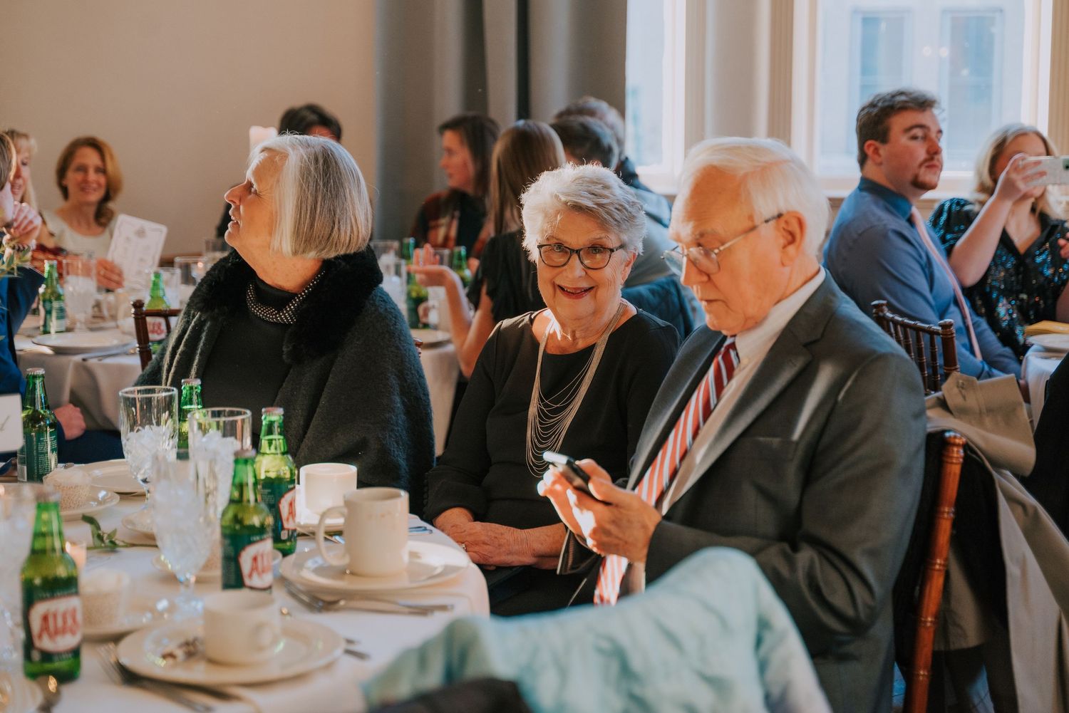 People seated at tables with drinks and place settings during what appears to be a formal dining event.