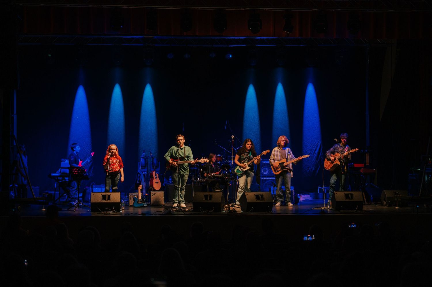 Musicians perform on stage with guitars under dramatic blue lighting during a live concert performance.