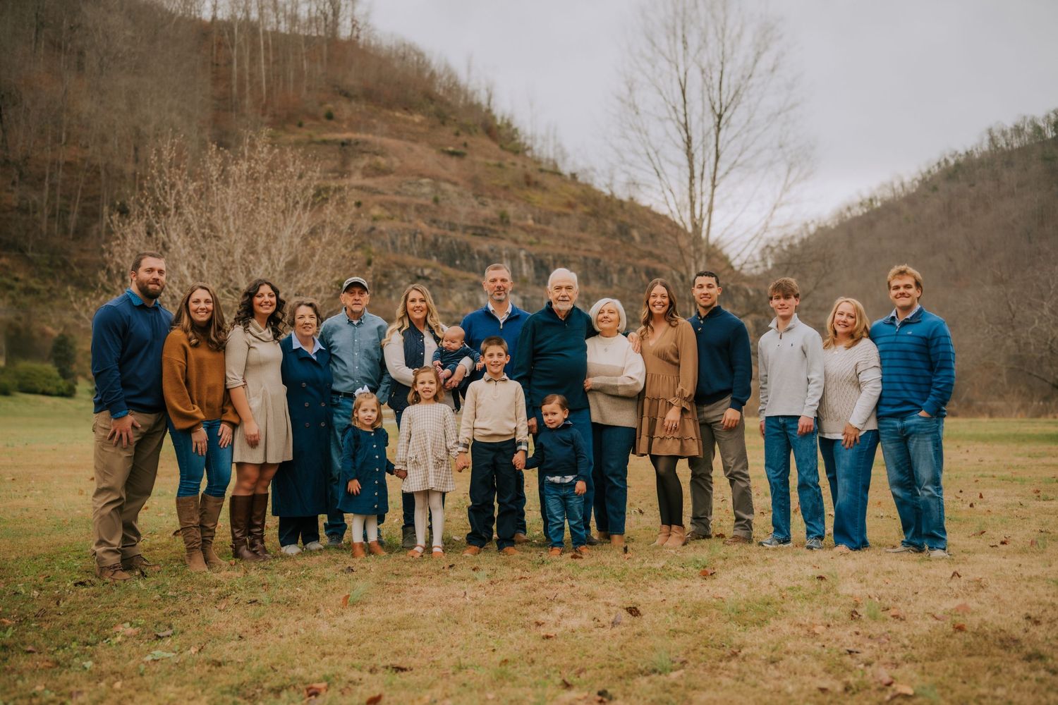 Extended family group portrait taken outdoors against a scenic hillside backdrop.