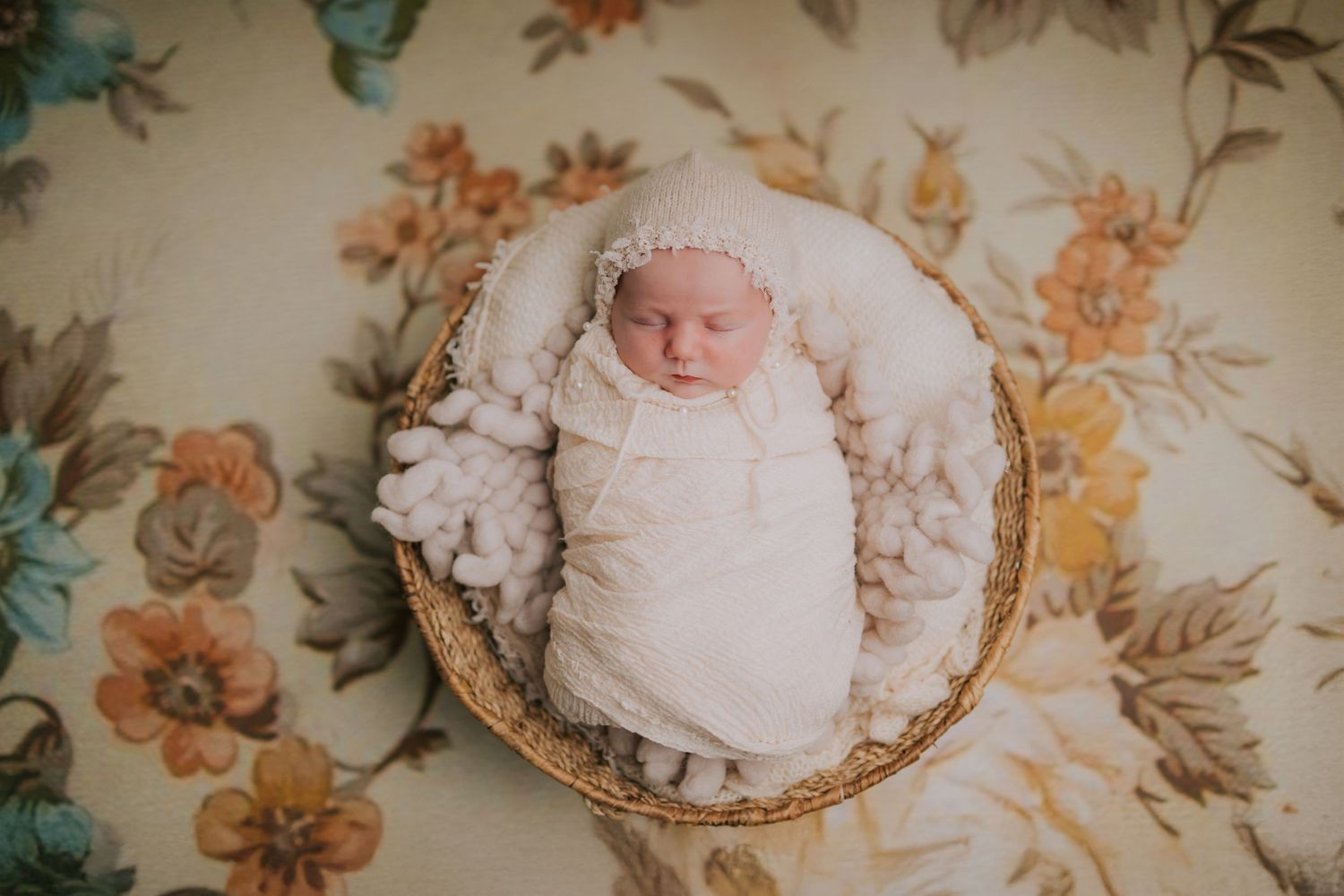 A sleeping infant rests peacefully on a floral patterned background.