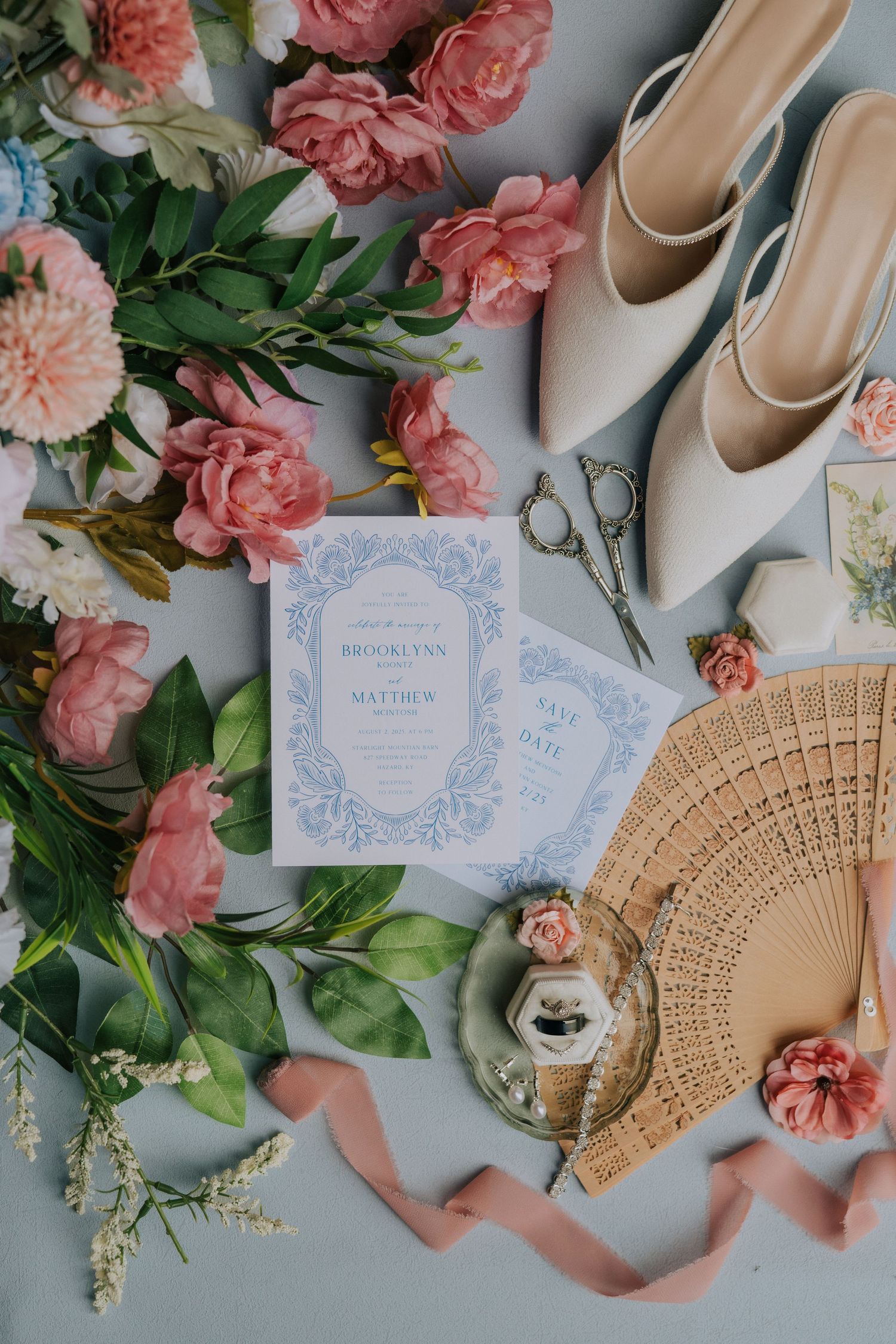 Wedding details flatlay with pink flowers, invitations, and bridal shoes.