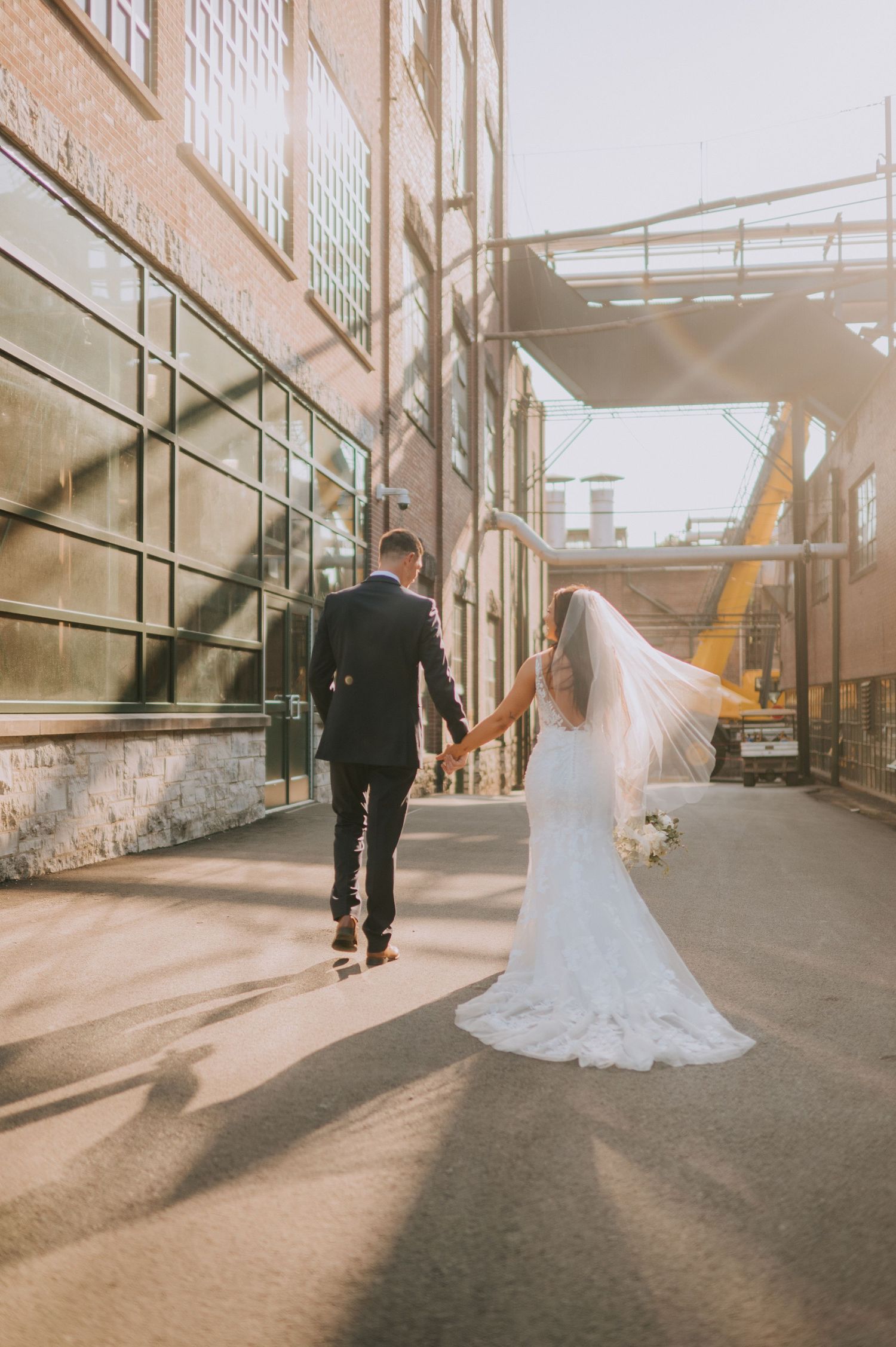 Wedding couple walking through industrial urban setting with dramatic shadows.