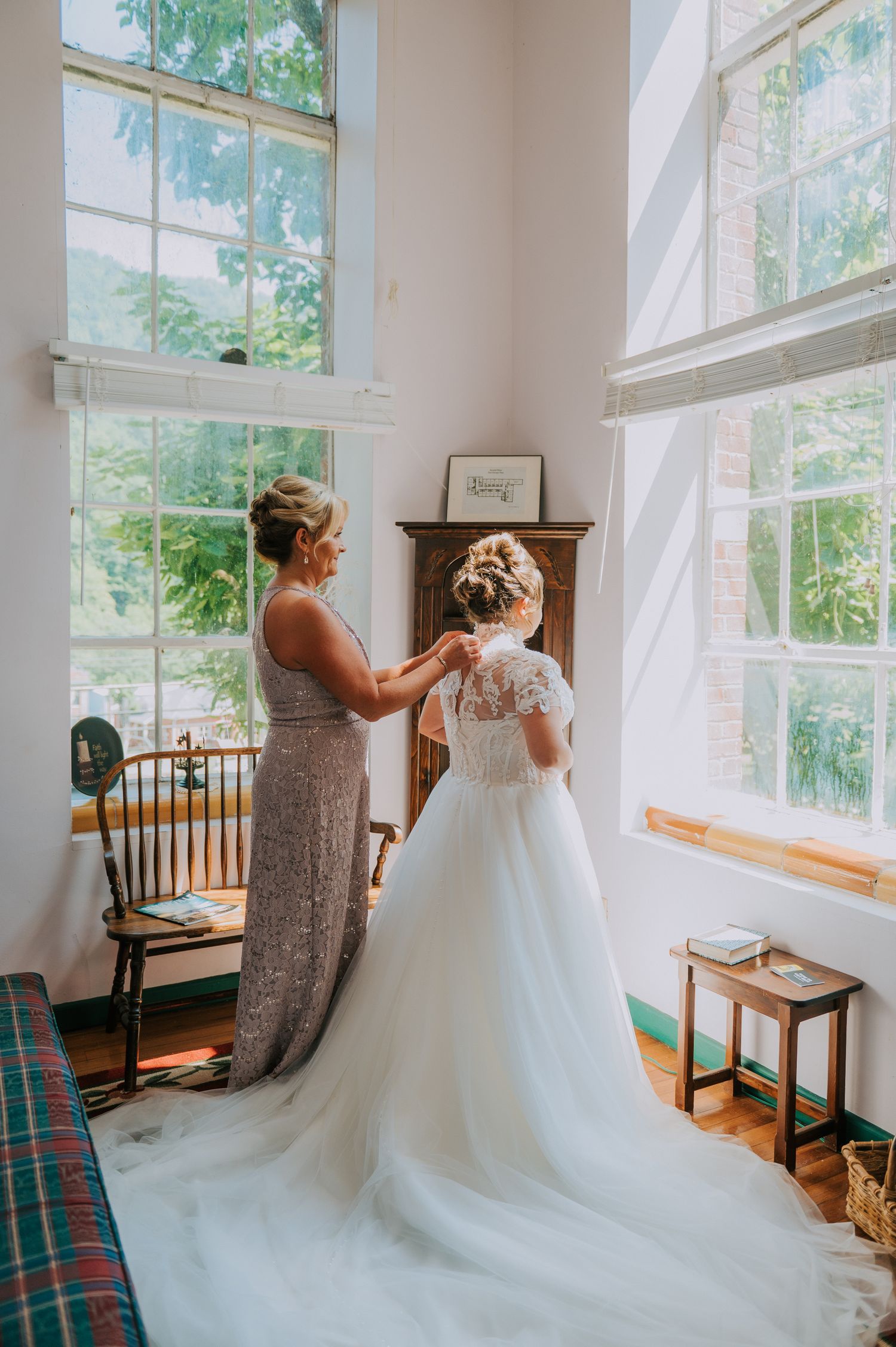 Sunlit bridal preparation room with large windows and white wedding gown.
