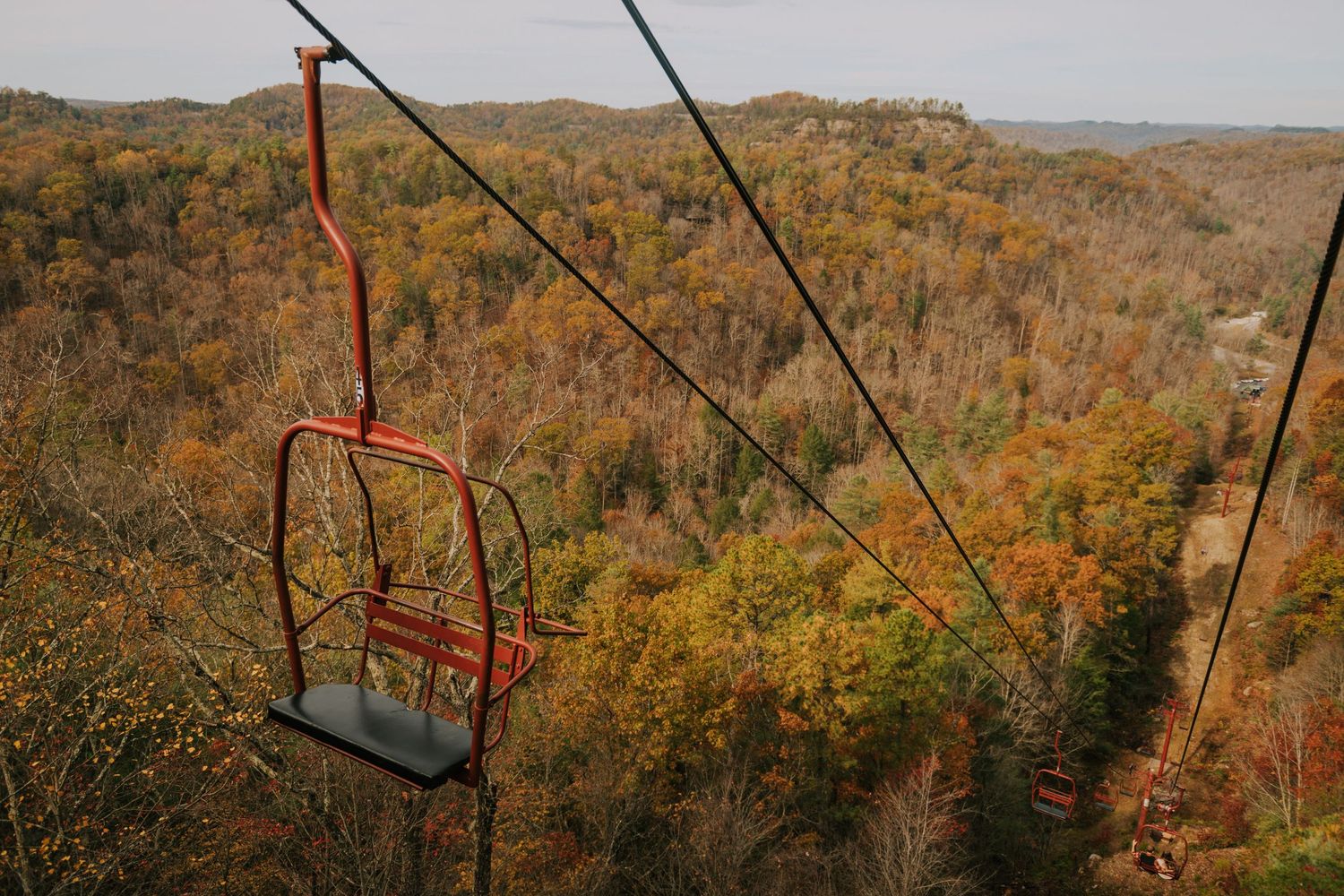 Ski lift cables stretch across a mountainous landscape painted in fall colors.