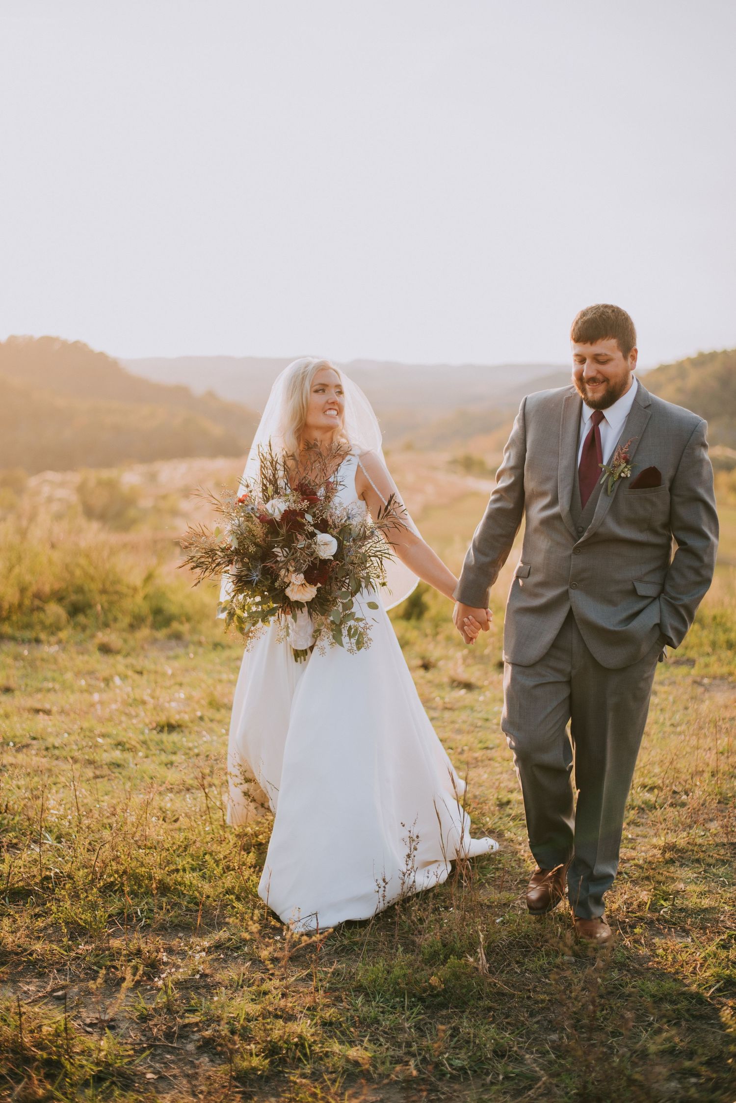Wedding couple traversing a hillside during golden hour with dramatic mountain views.