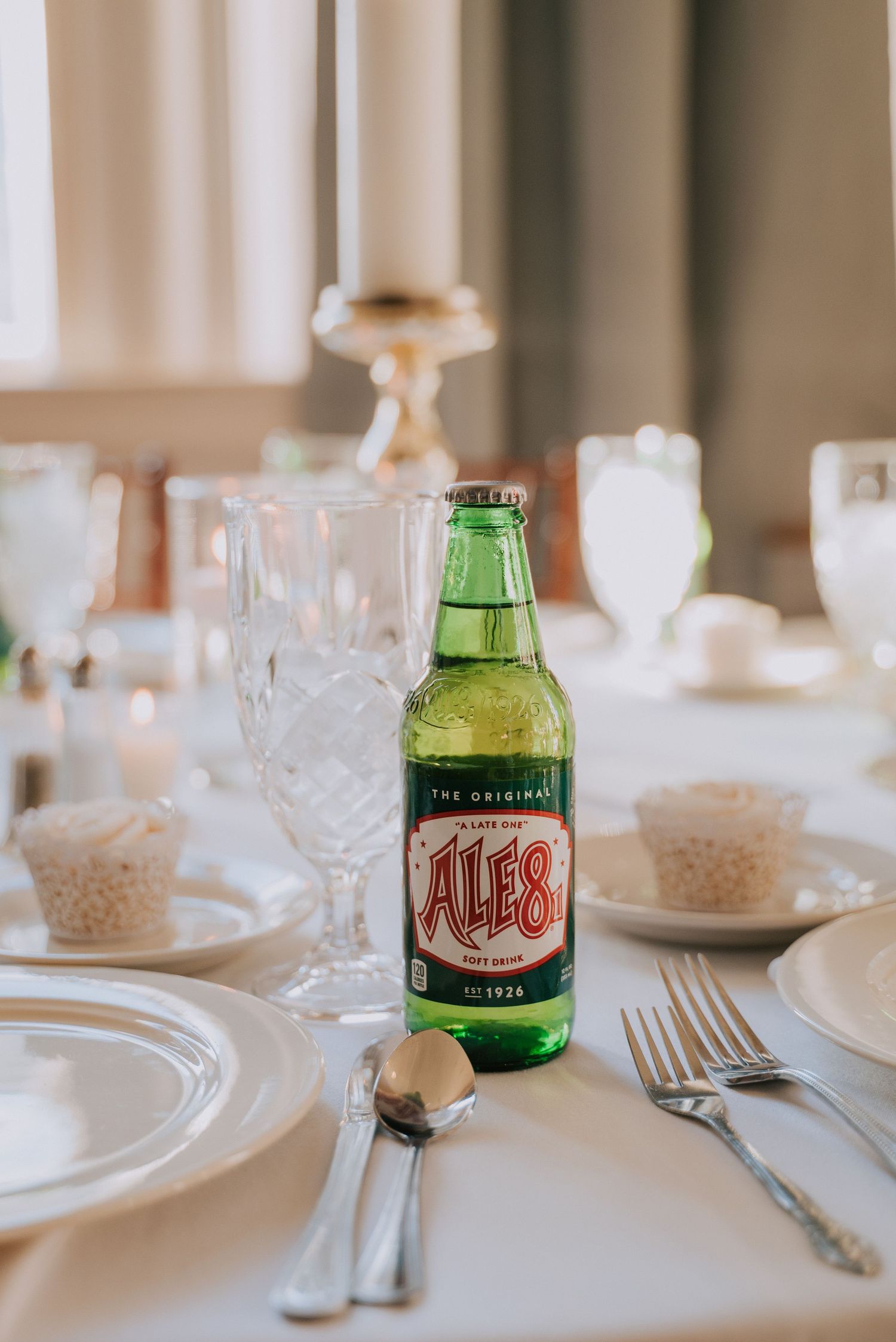 Place setting at wedding reception with Ale-8-One soda bottle and crystal glassware on white tablecloth.