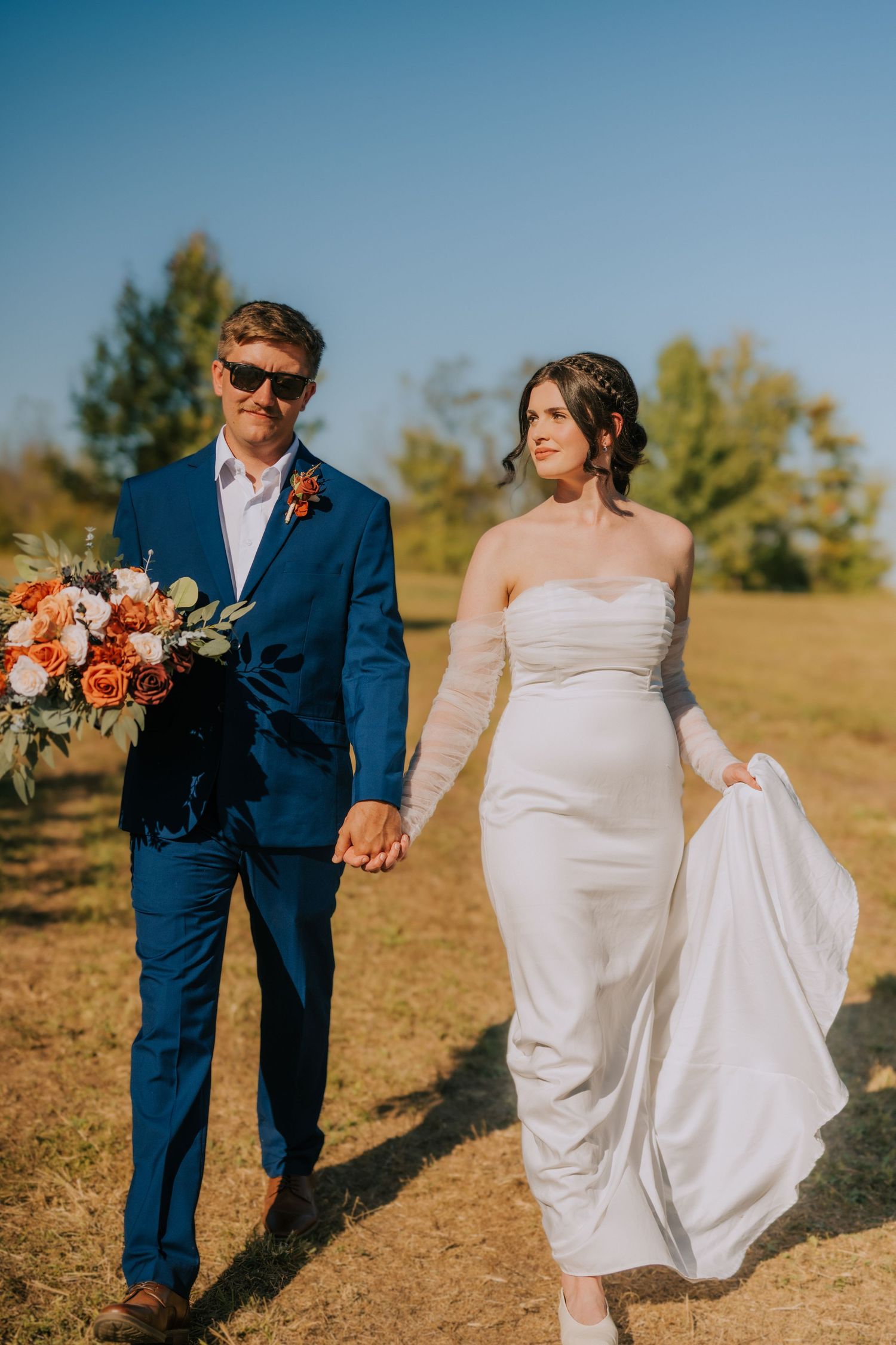 A romantic outdoor wedding photoshoot featuring couples in white dresses and navy suits against a golden field backdrop.