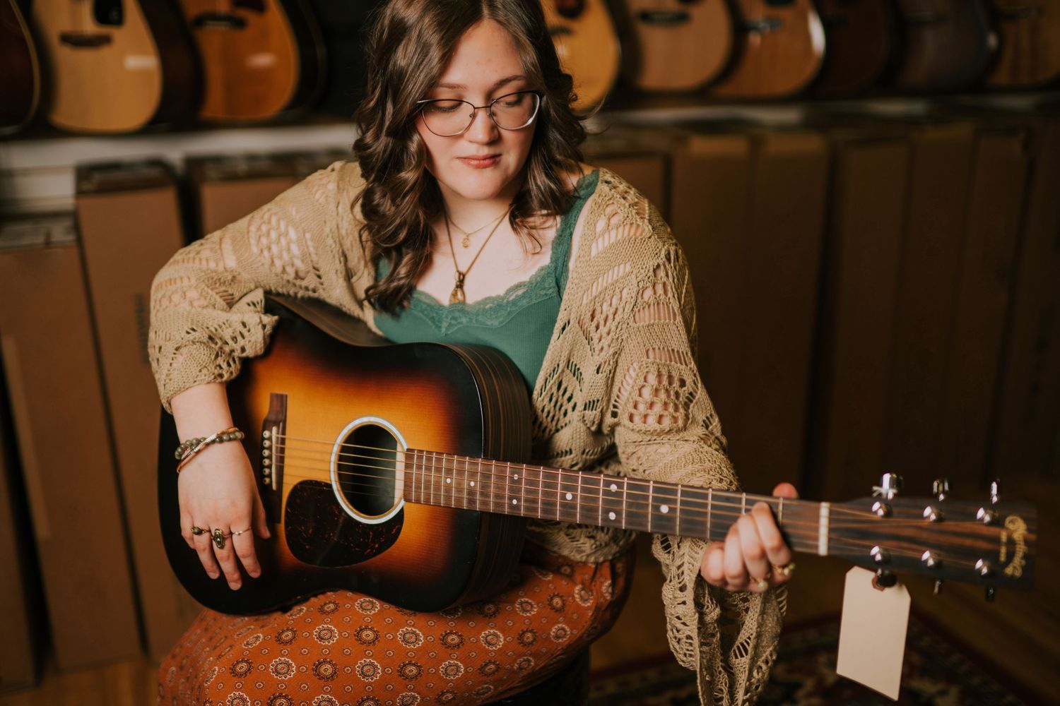 Musician playing acoustic guitar while wearing a knit cardigan and patterned skirt.