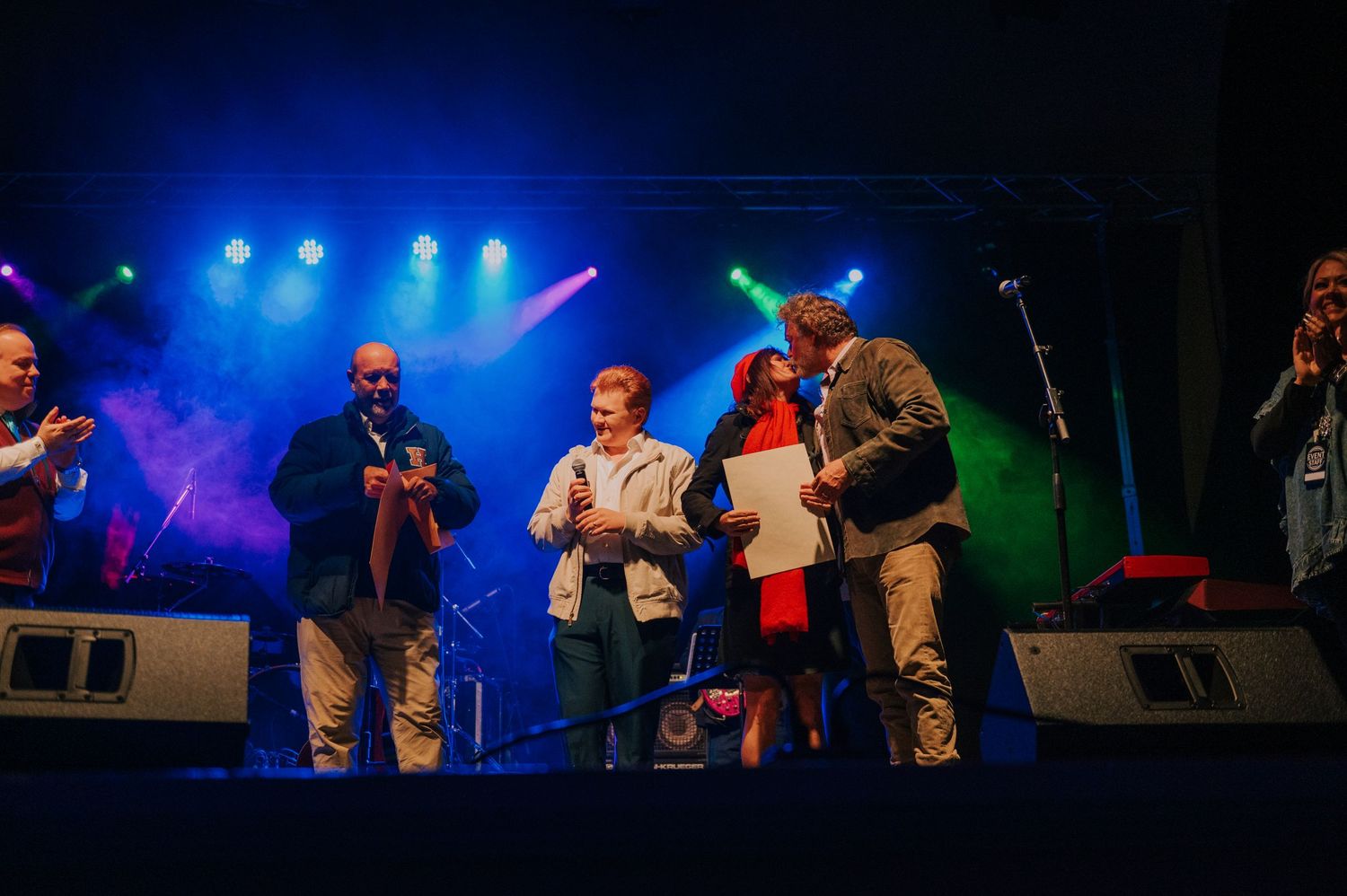 Musicians perform together on stage with dramatic blue and green concert lighting illuminating the performance.