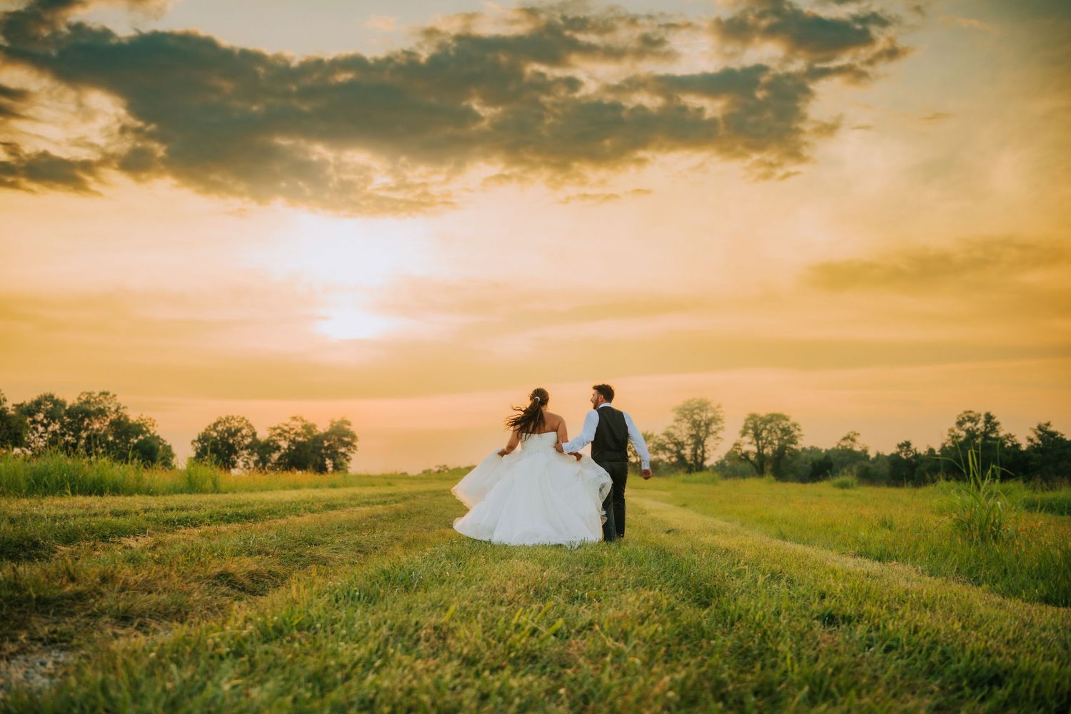 Silhouettes of a couple stand together in golden sunset light across rolling meadow landscapes.