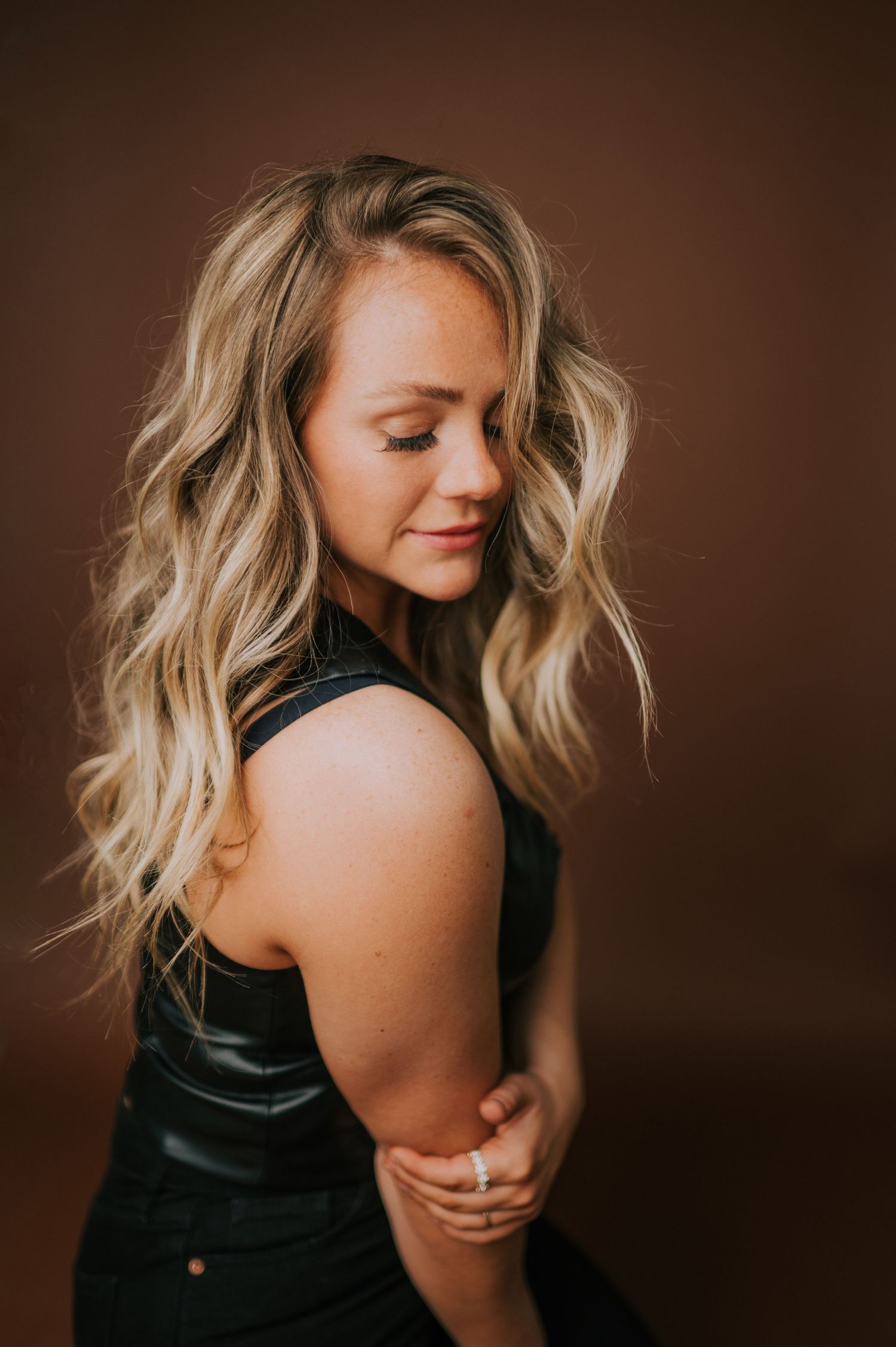 Artistic boudoir photography with dramatic lighting against brown backdrop.