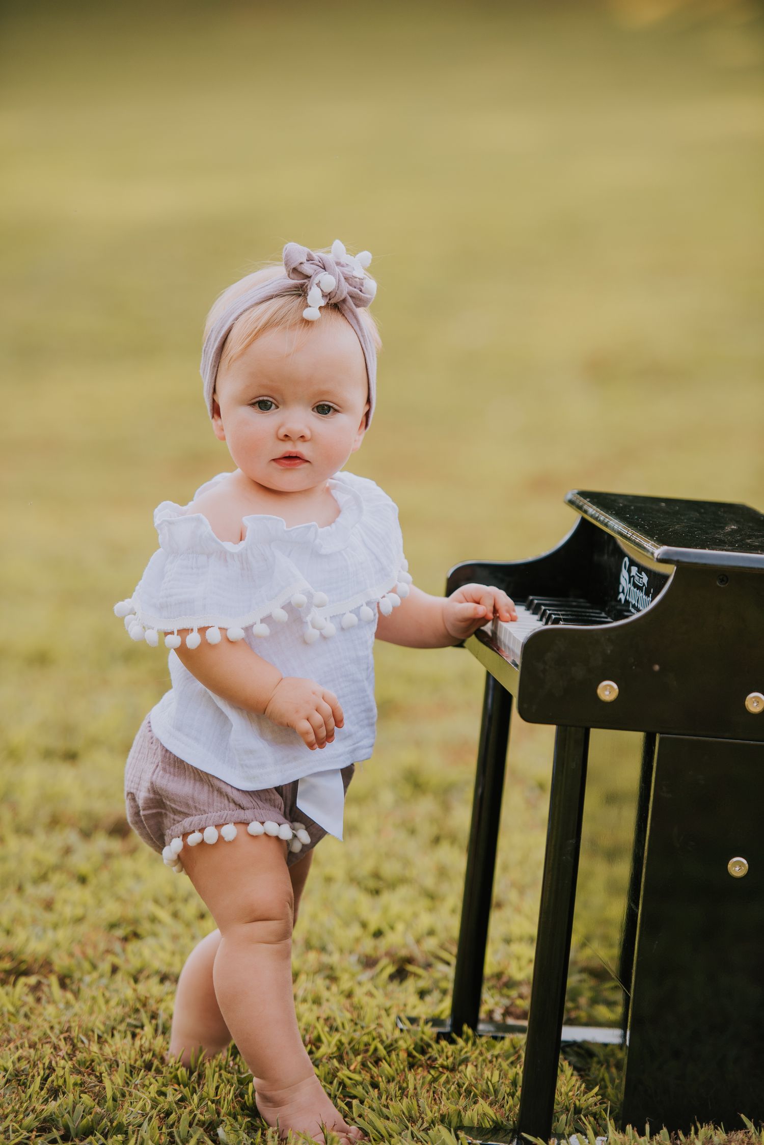 Small child in white dress playing with black furniture on grassy lawn.
