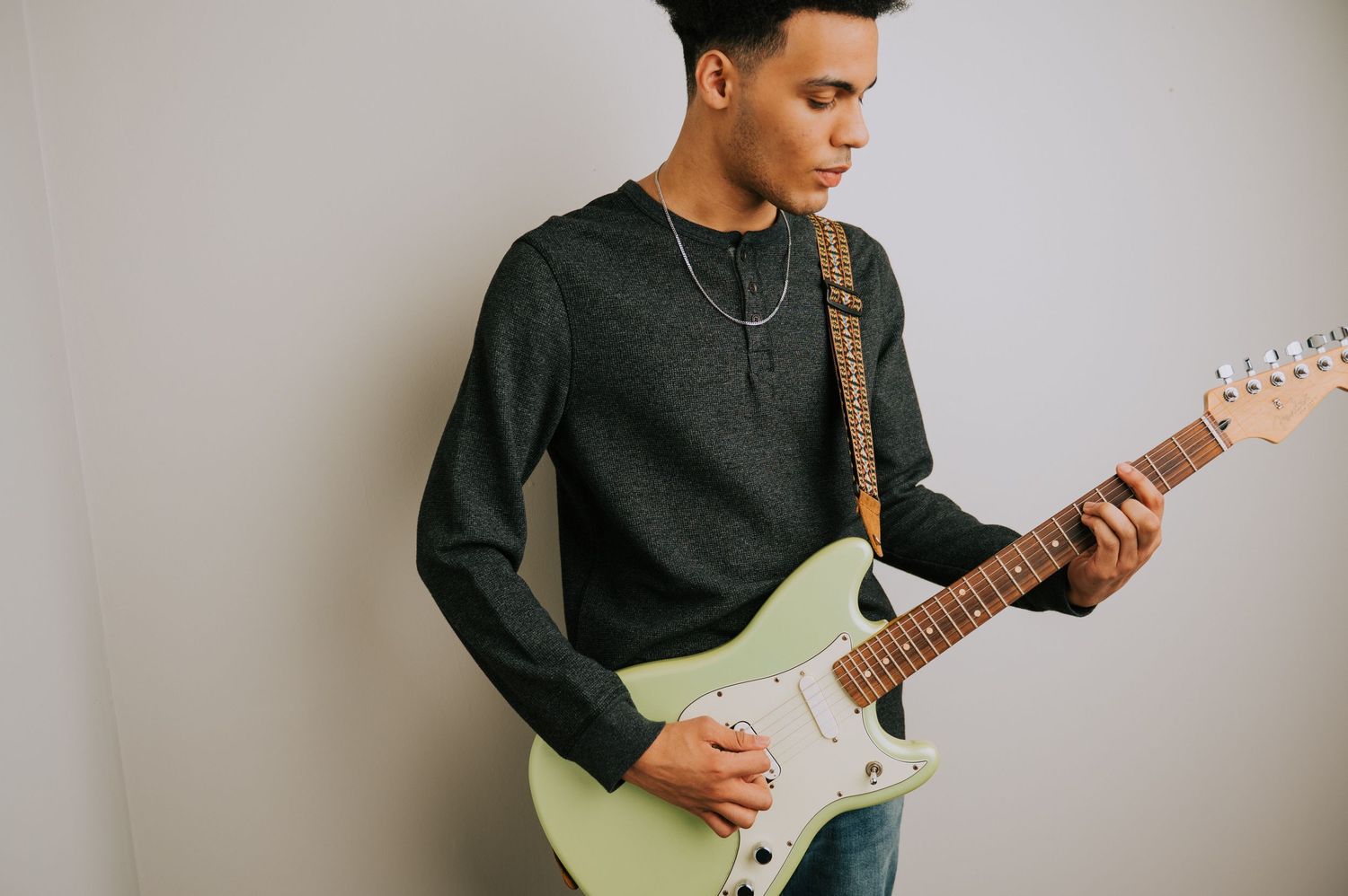 Person in black clothing playing a mint green electric guitar against a white background.