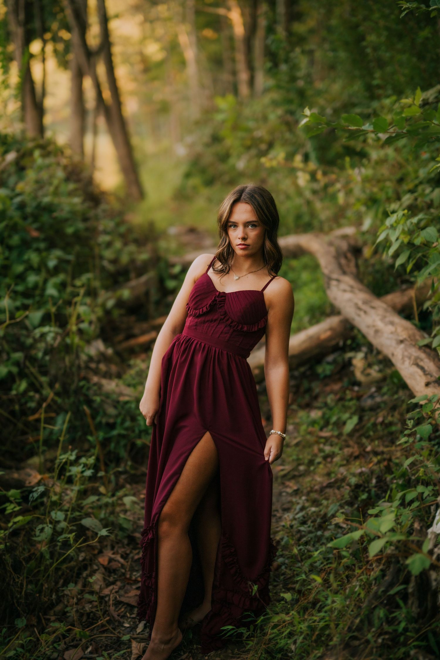 Ethereal forest photography series in burgundy dress among lush greenery.