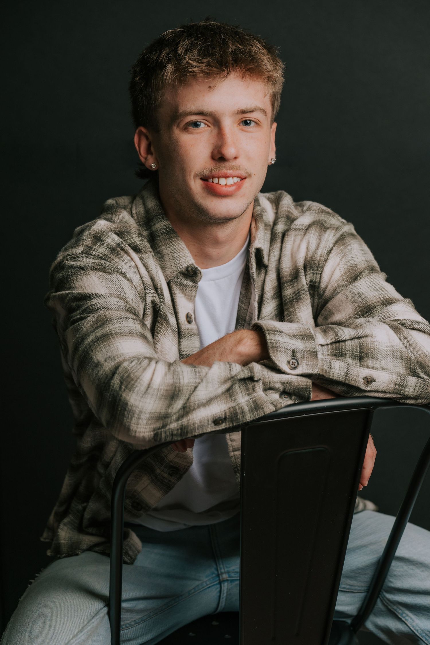 Student poses casually in plaid jacket against dark studio background.