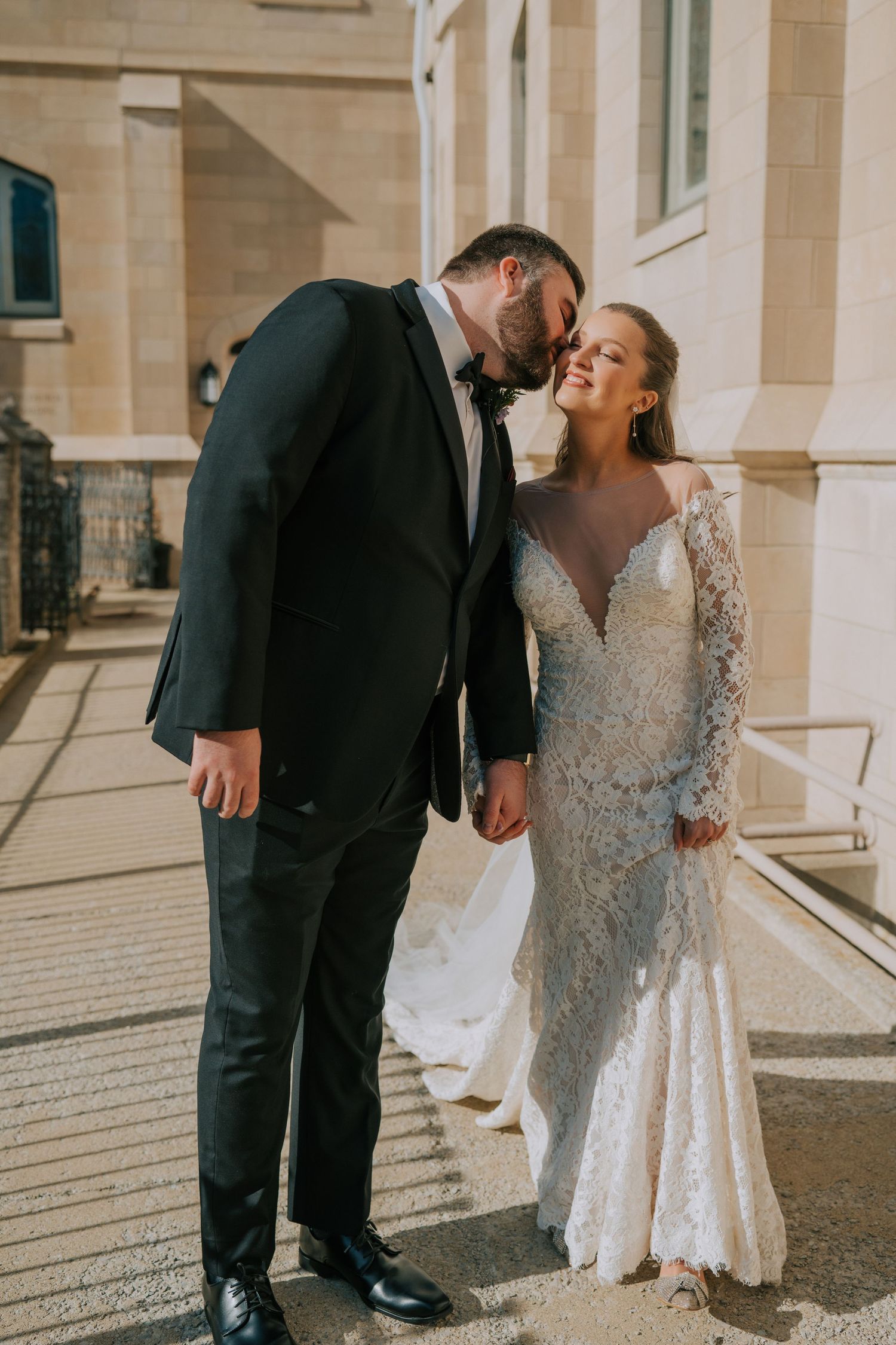 A romantic wedding moment captured outside a stone building featuring elegant formal attire.