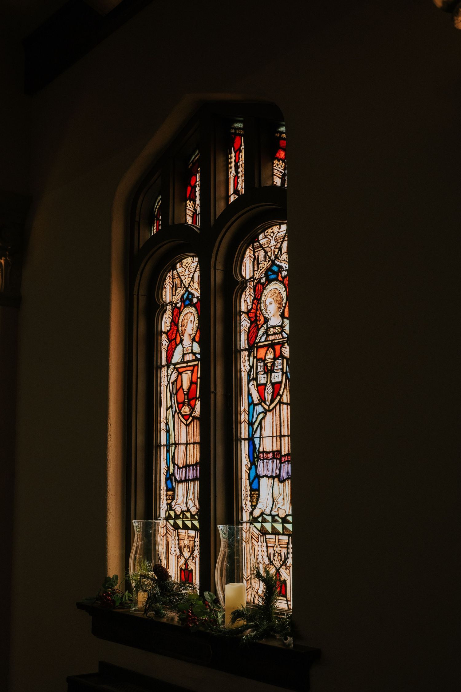 Ornate stained glass church windows with religious figures cast warm light into a darkened interior.
