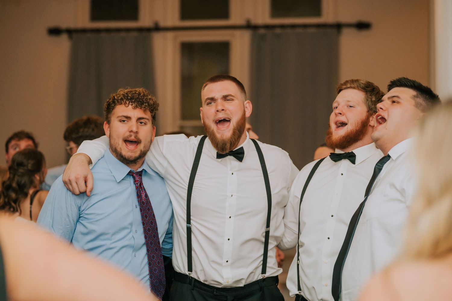 Wedding guests enjoying a fun moment together in suspenders and bow ties at a reception.
