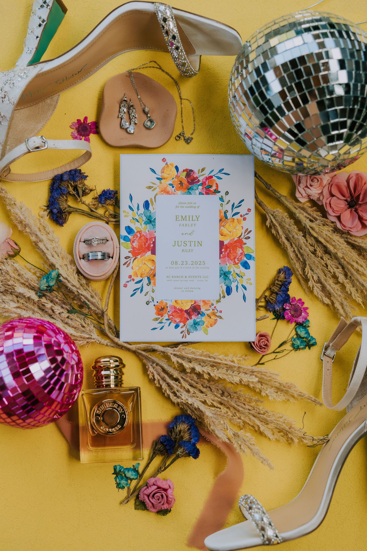 Wedding invitation with floral design surrounded by disco balls, flowers and bridal accessories on yellow background.