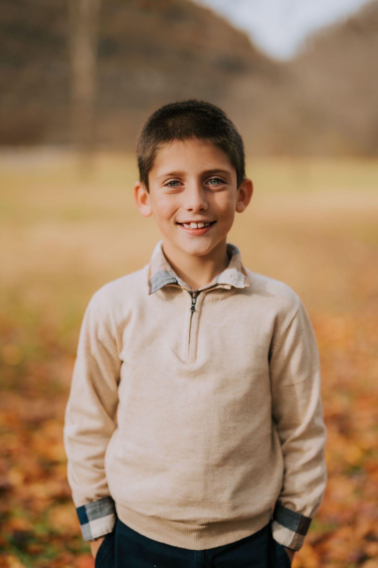 Child in beige quarter-zip sweater photographed in autumn setting.
