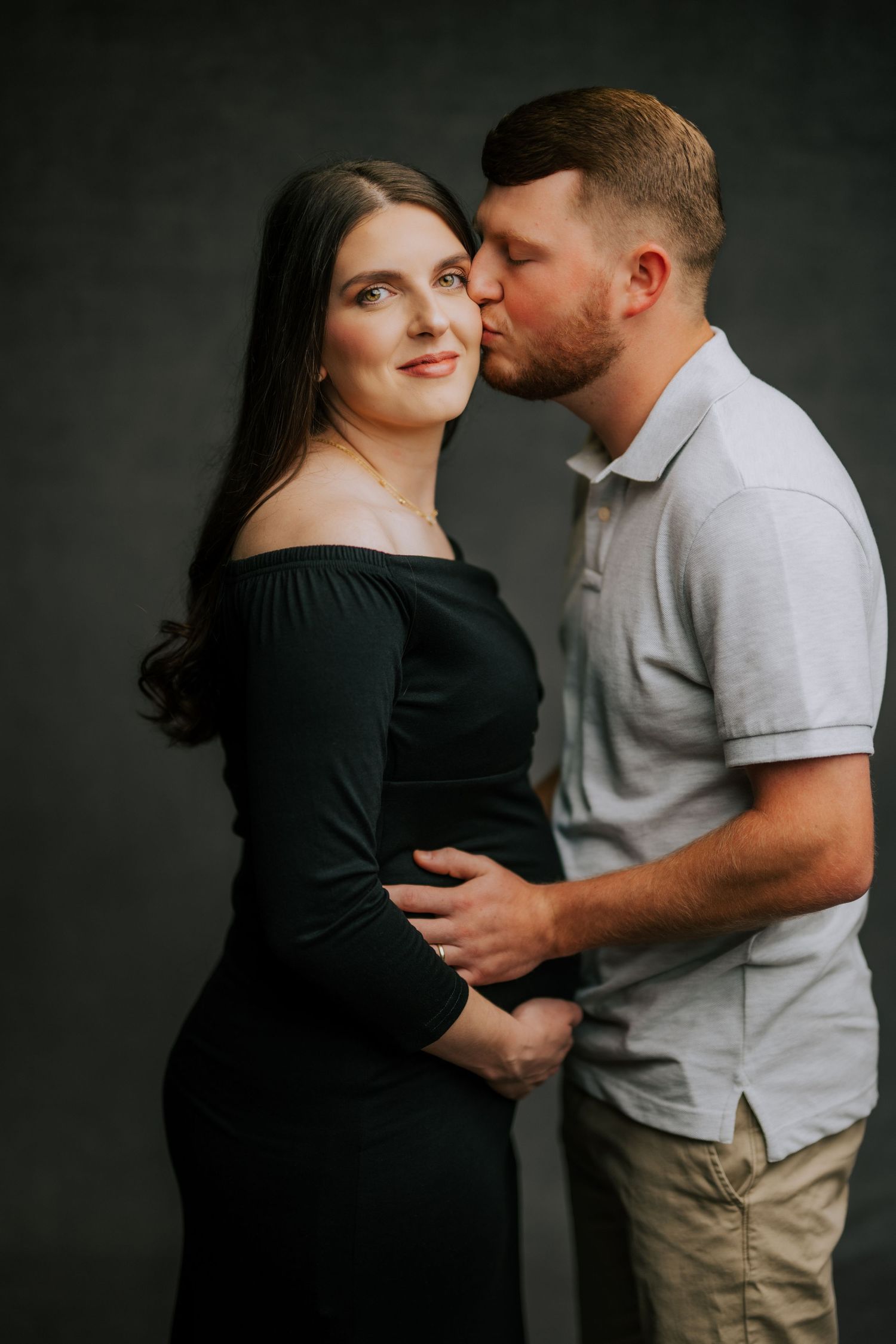 Intimate maternity portrait of couple in black and grey against dark background.