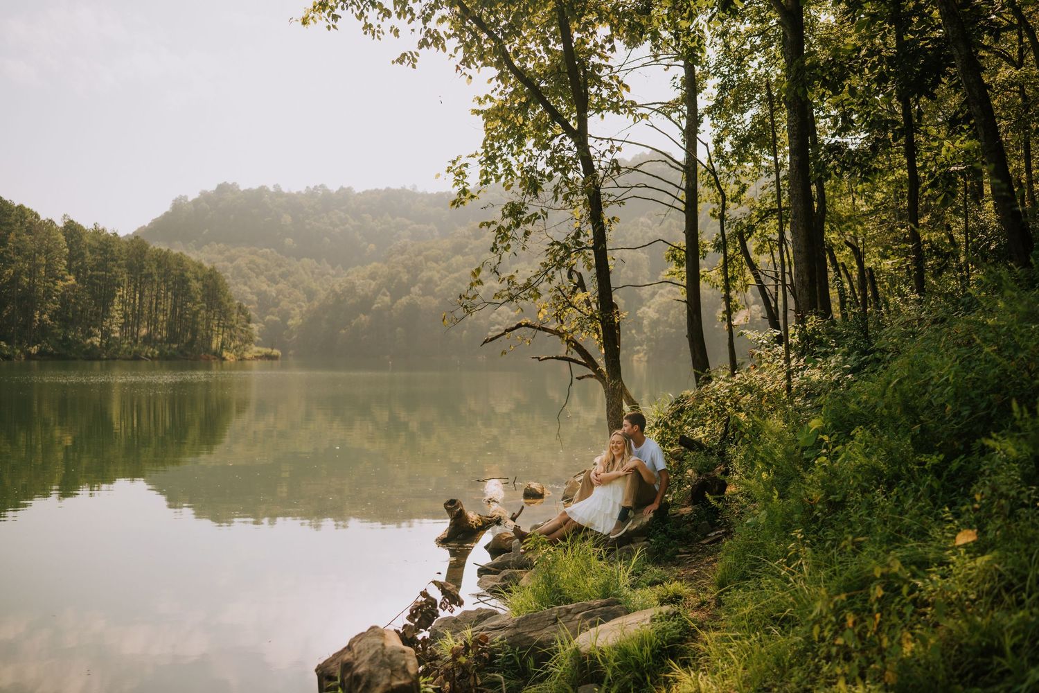 Scenic lakeside photo session with couple surrounded by trees and water views.