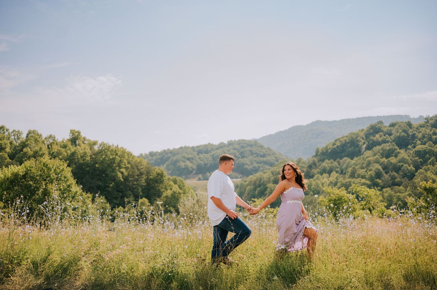 A couple dances together in a sun-lit mountain meadow surrounded by tall grass.