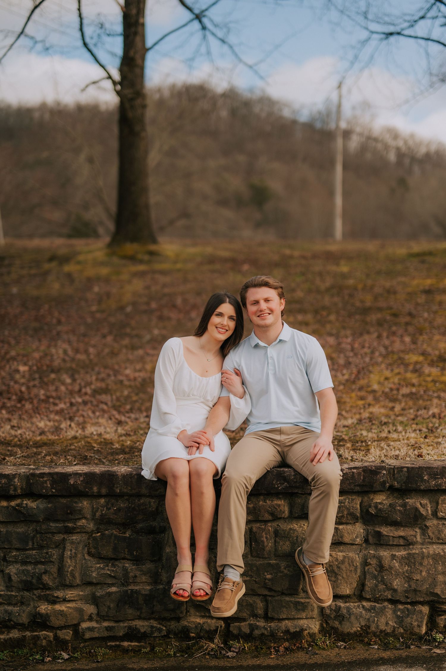 Couple sitting together on stone wall during outdoor photo session.