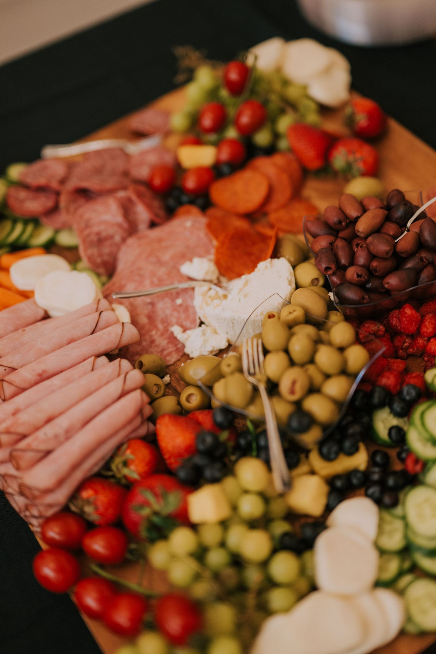 Close-up view of a charcuterie board with assorted meats, olives, cherry tomatoes, and fresh vegetables arranged artfully.