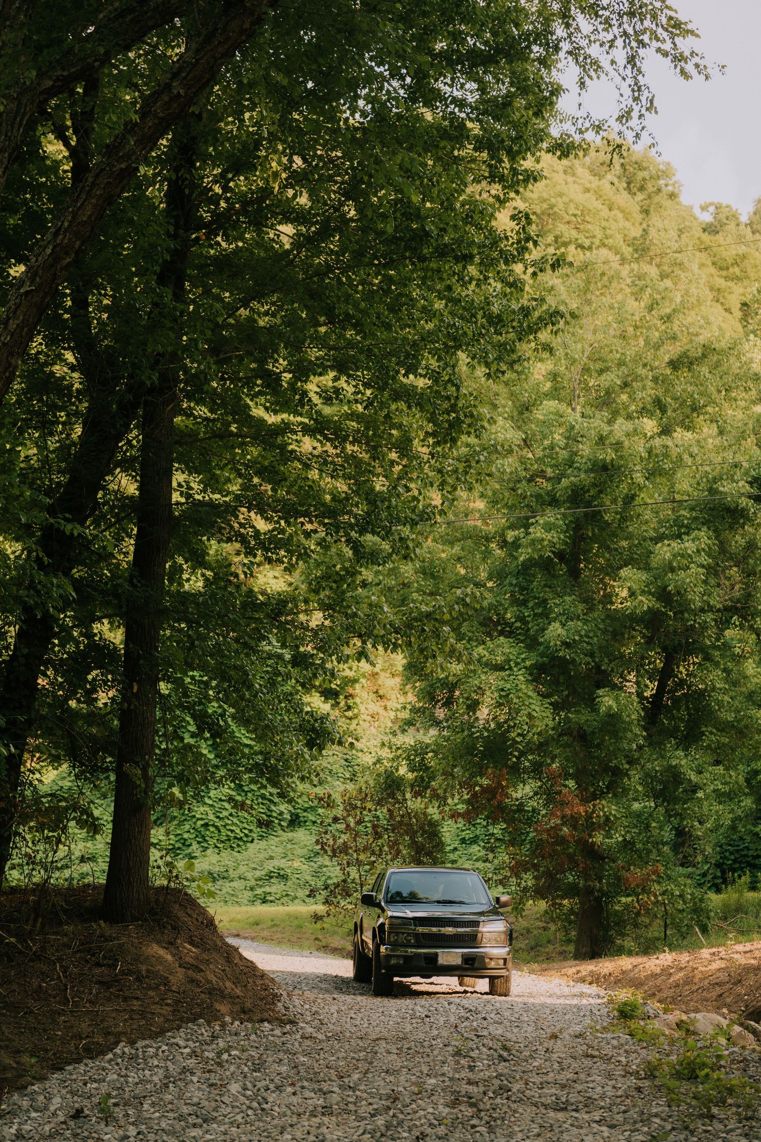 A dark pickup truck parked on a gravel path surrounded by lush green trees in a serene forest setting.