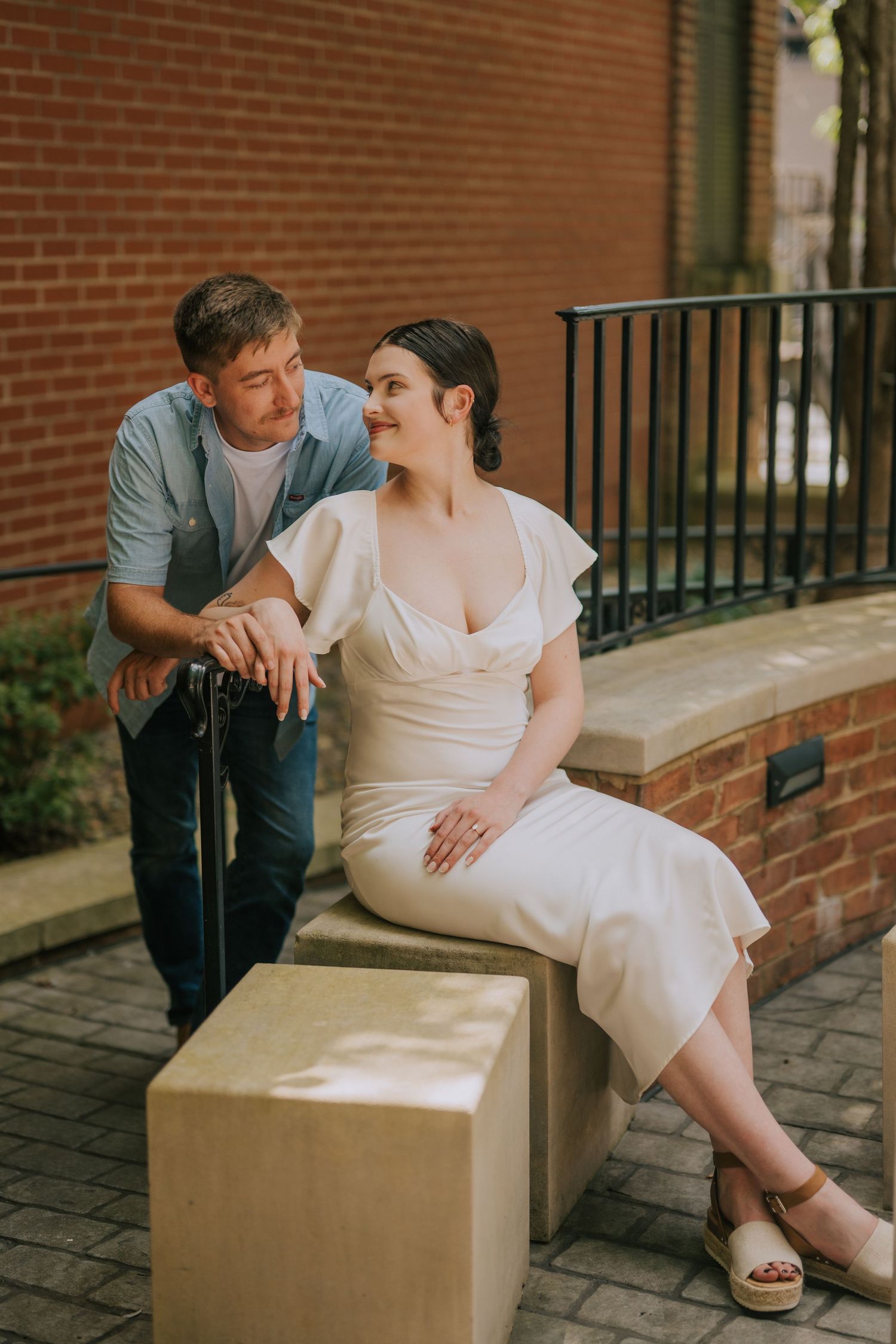 Couple sitting together on stone bench against red brick wall during photo session.