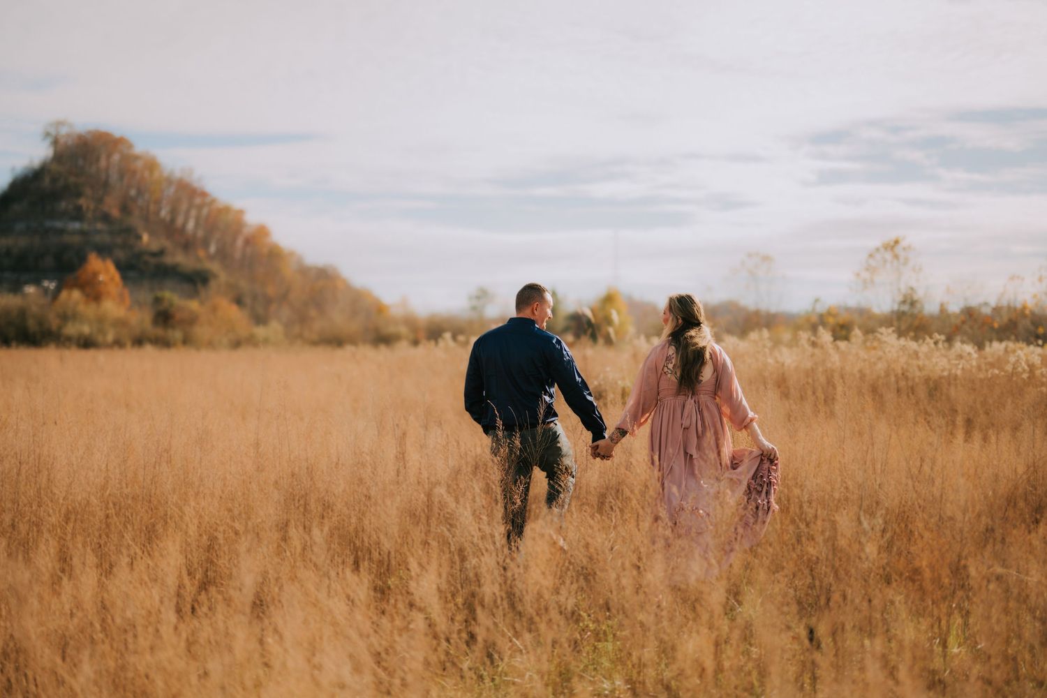 Couple walking through a golden wheat field during sunset.