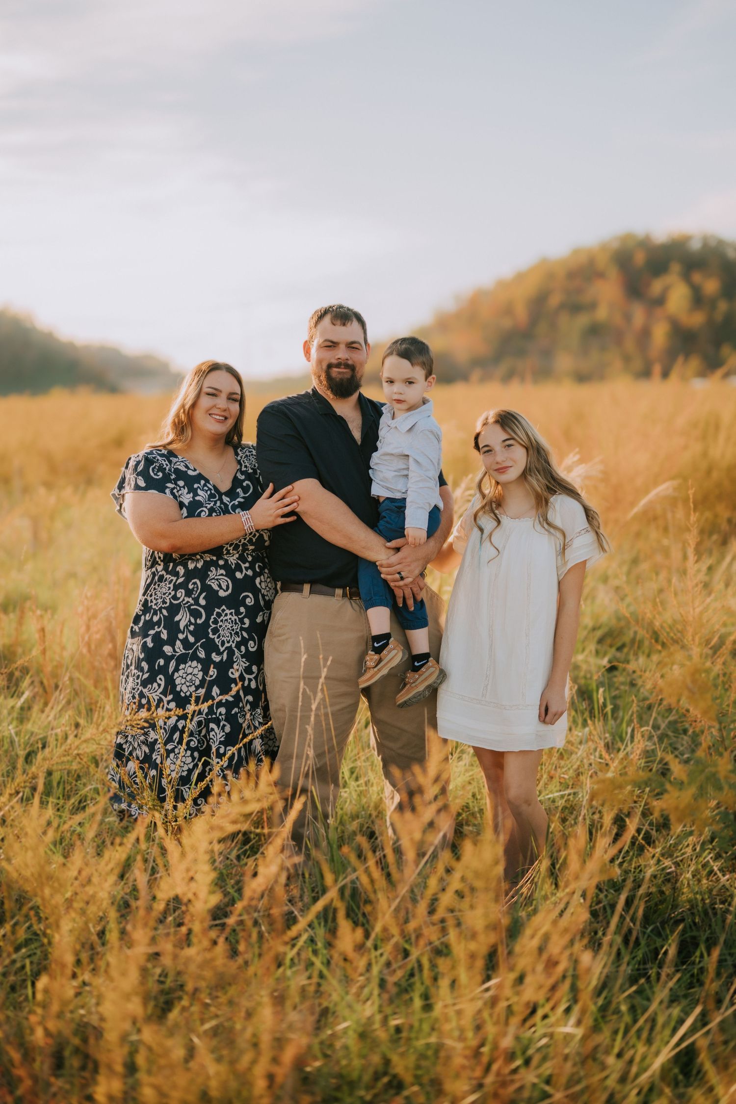 Family walking together through tall golden grass at sunset.