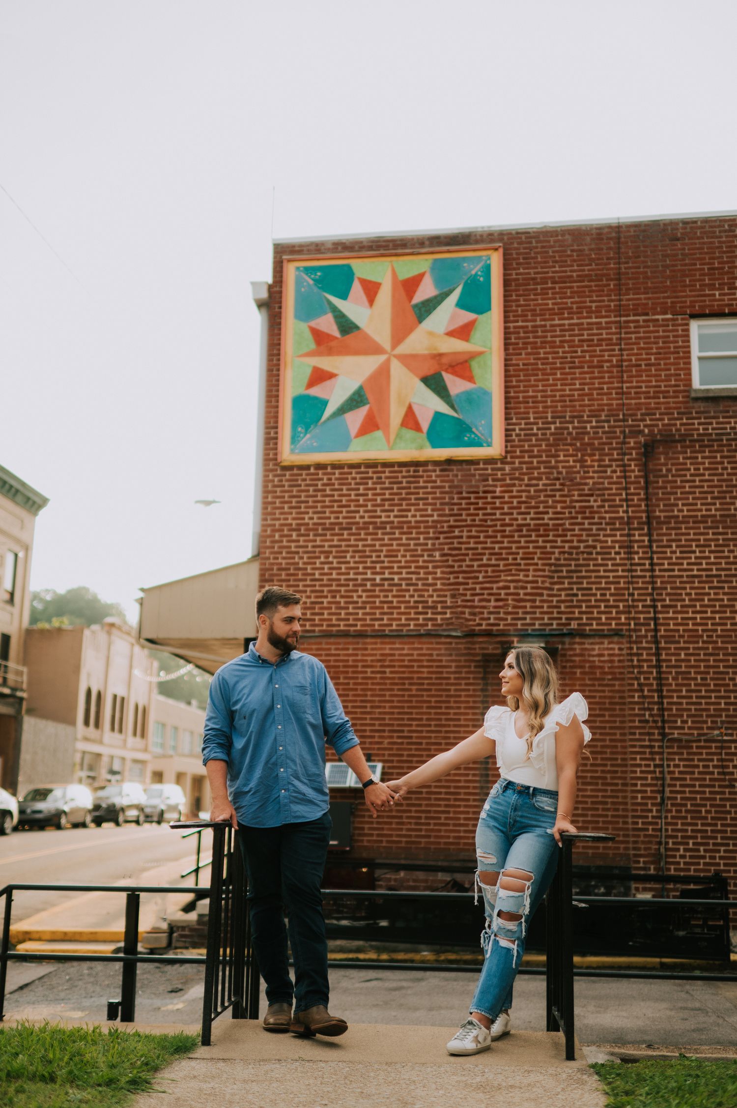 A couple strolls past a brick building with colorful quilt-pattern artwork.