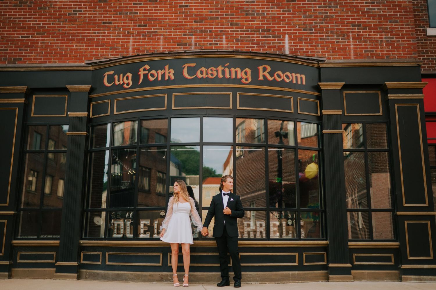 A couple poses outside the Cup Fork Tasting Room with classic brick storefront architecture.