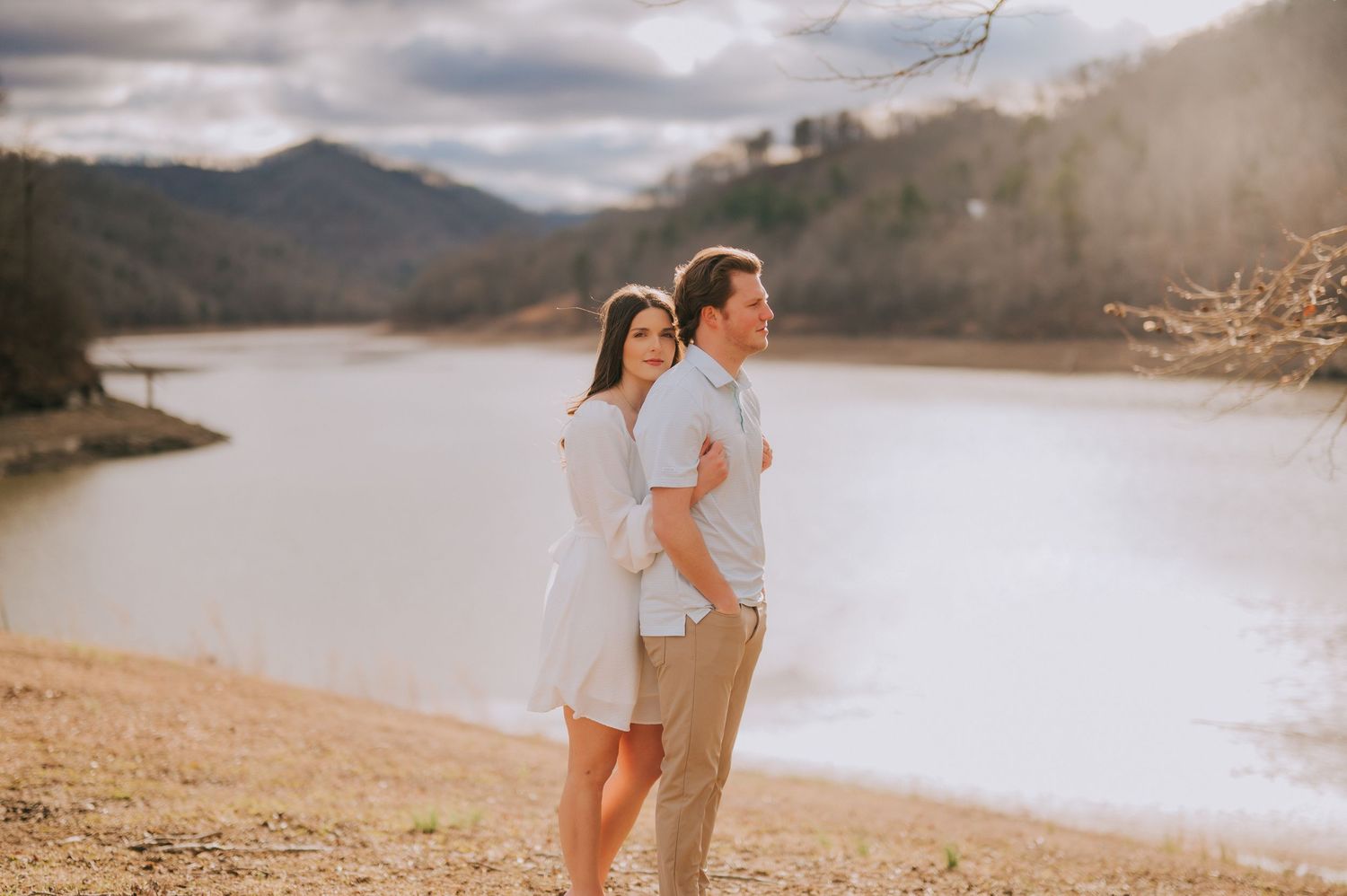 A couple shares romantic moments along a scenic mountain lake during golden hour.