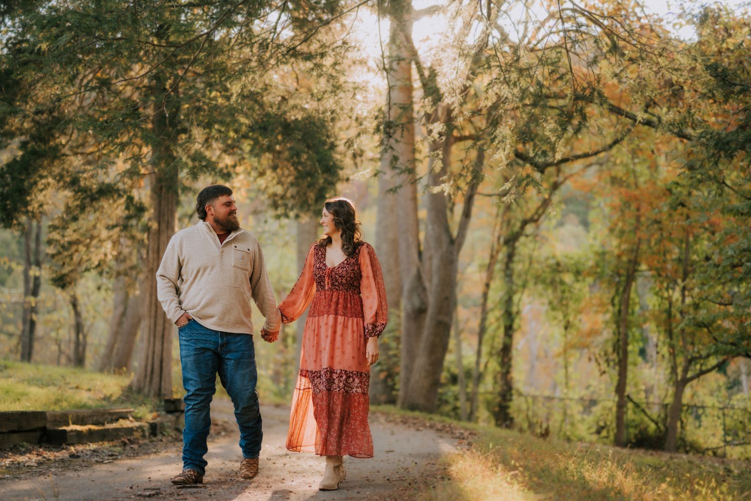 Couple walking through autumn trees on nature path during fall photoshoot.