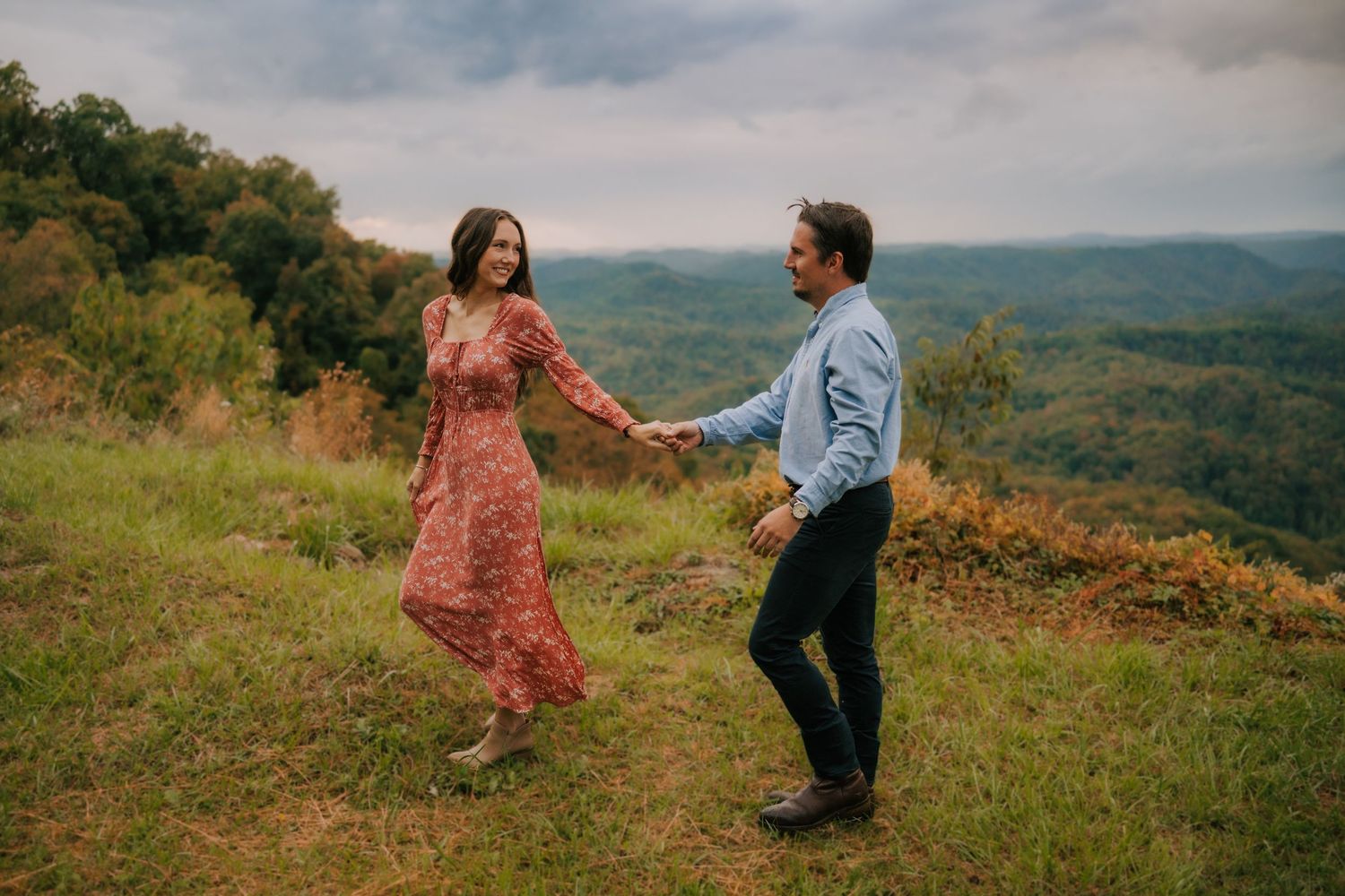 Couple dancing playfully on grassy hilltop with mountain views.