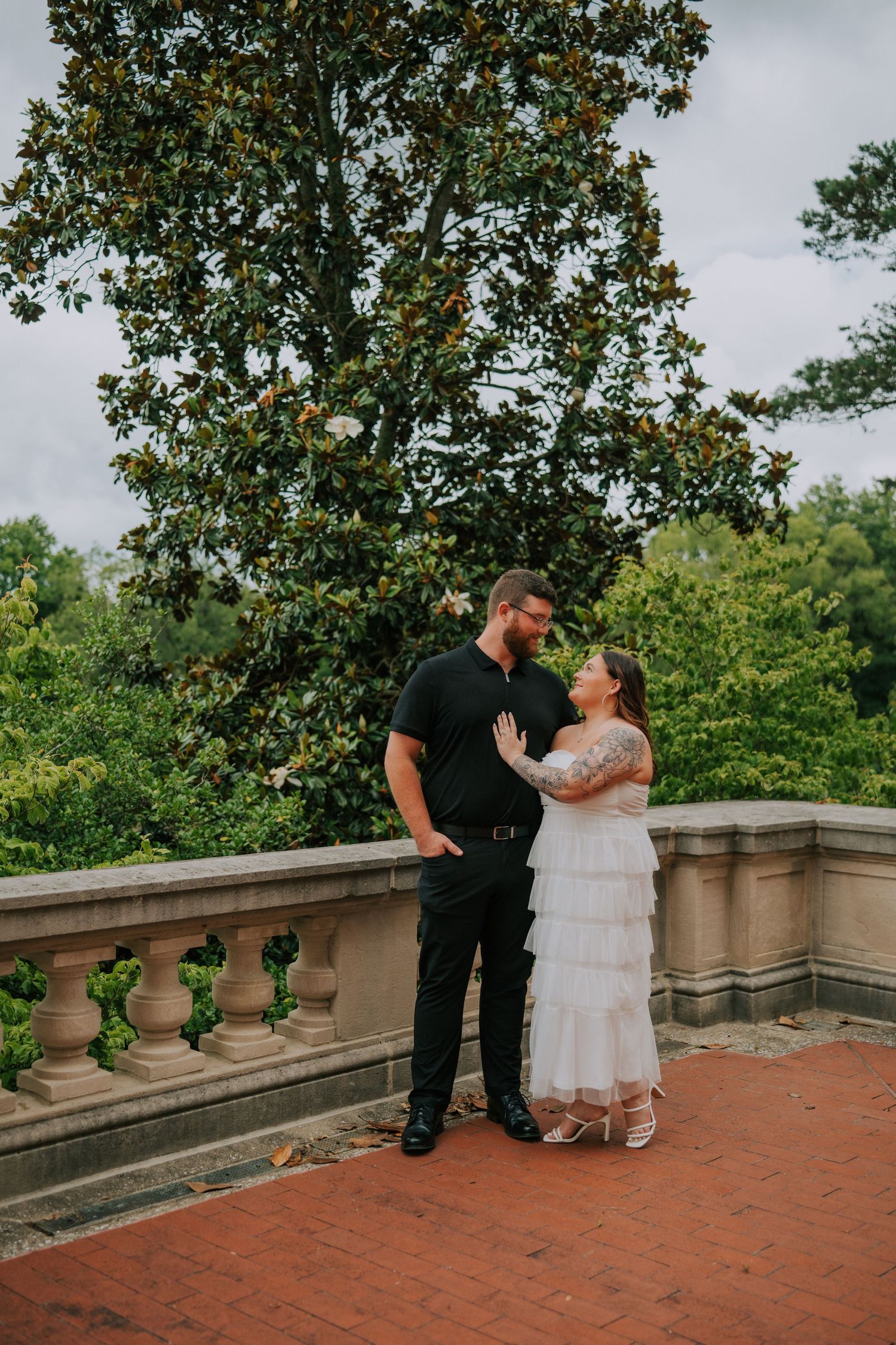 A couple shares an intimate moment on a brick terrace with stone balustrades.