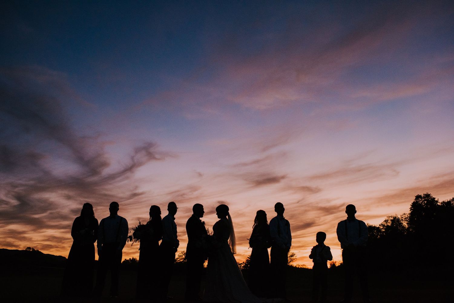 Silhouettes of wedding guests against a dramatic sunset sky.